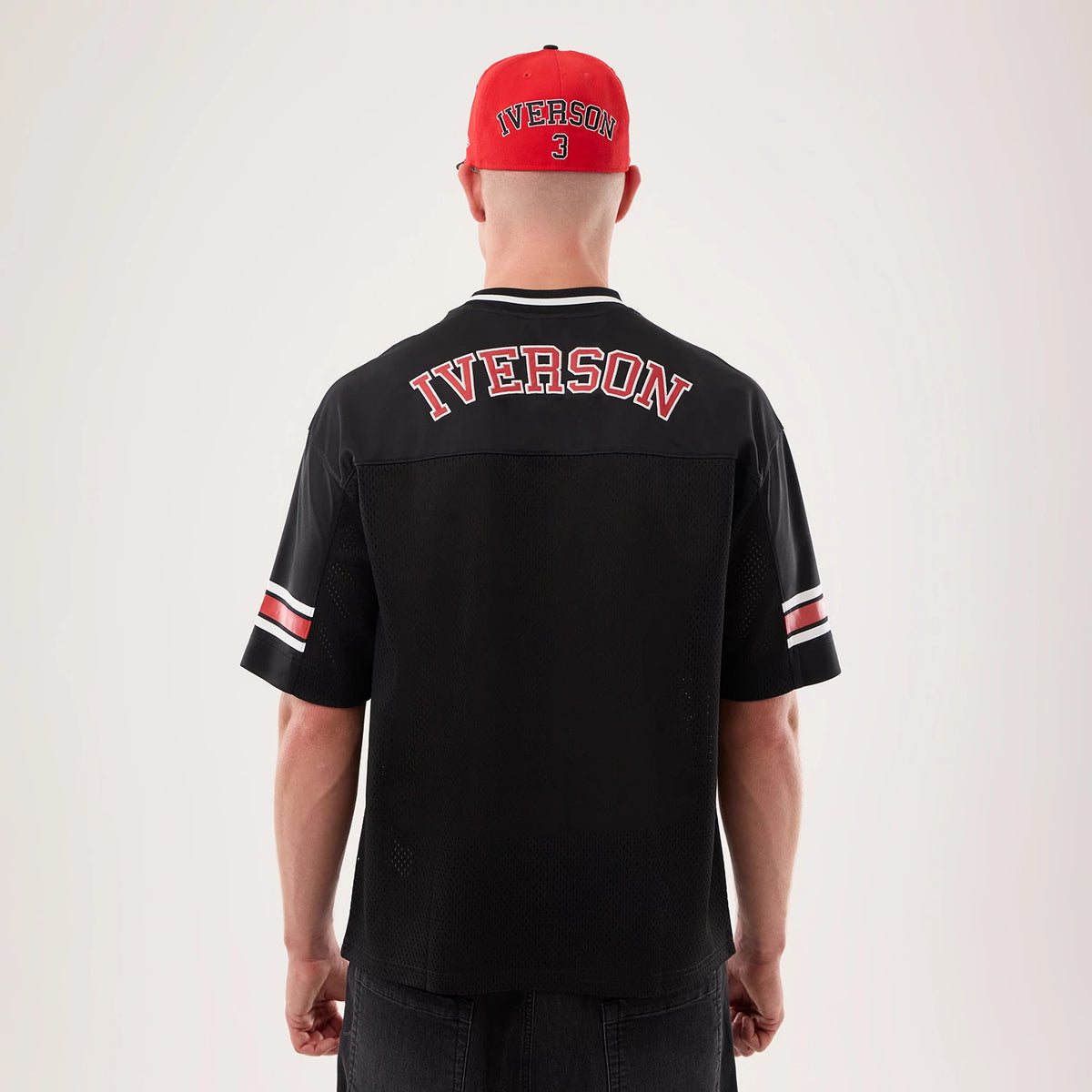 New Era Philadelphia 76ers NBA Hardwood Classic Mesh Oversized Black T-Shirt, back view on a model wearing a red cap, showing Iverson lettering in red and white across the upper back, and distinct red and white stripes on the sleeves.