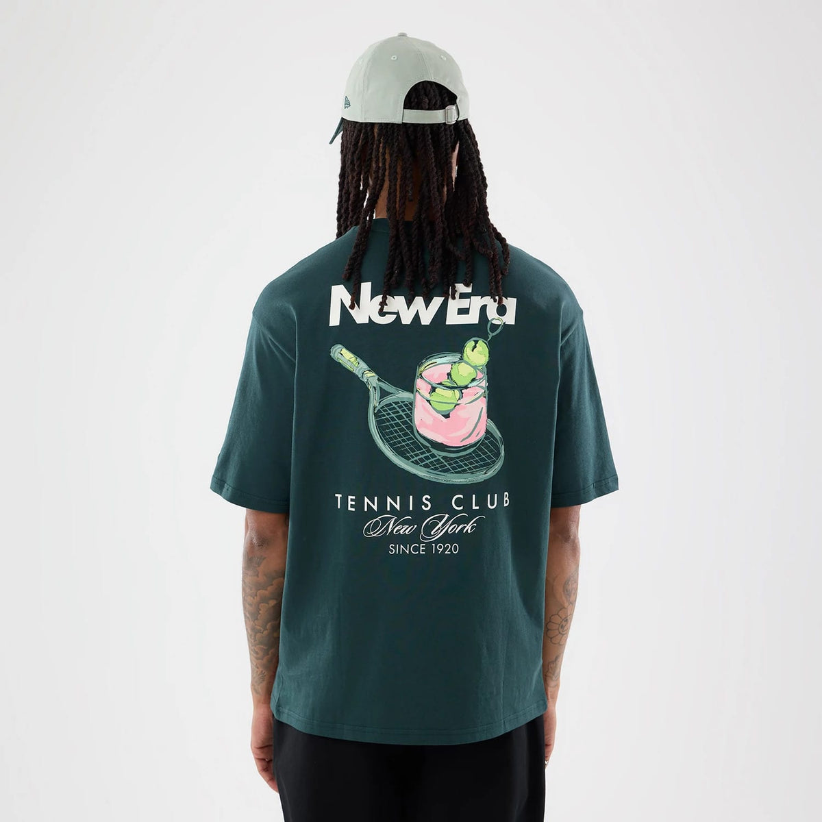 The model is wearing this New Era Tennis Graphic Oversized T-Shirt in dark green. 2