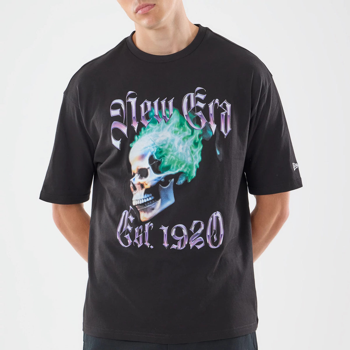 New Era Skull Graphic Oversized Black T-Shirt, front view on-model showcasing a skull graphic with green flames and purple New Era lettering across the chest, small embroidered New Era logo on the left sleeve.