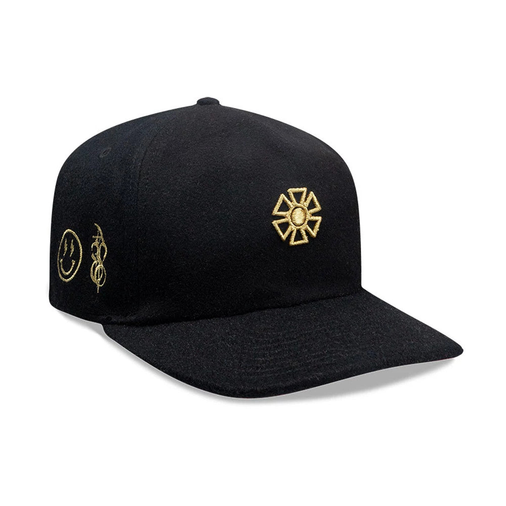 New Era X Omerta Balvin Black 19TWENTY Adjustable Cap, front view showing a gold embroidered geometric logo on the front panel, with additional gold smiley face and abstract designs on the side, and a curved black visor.