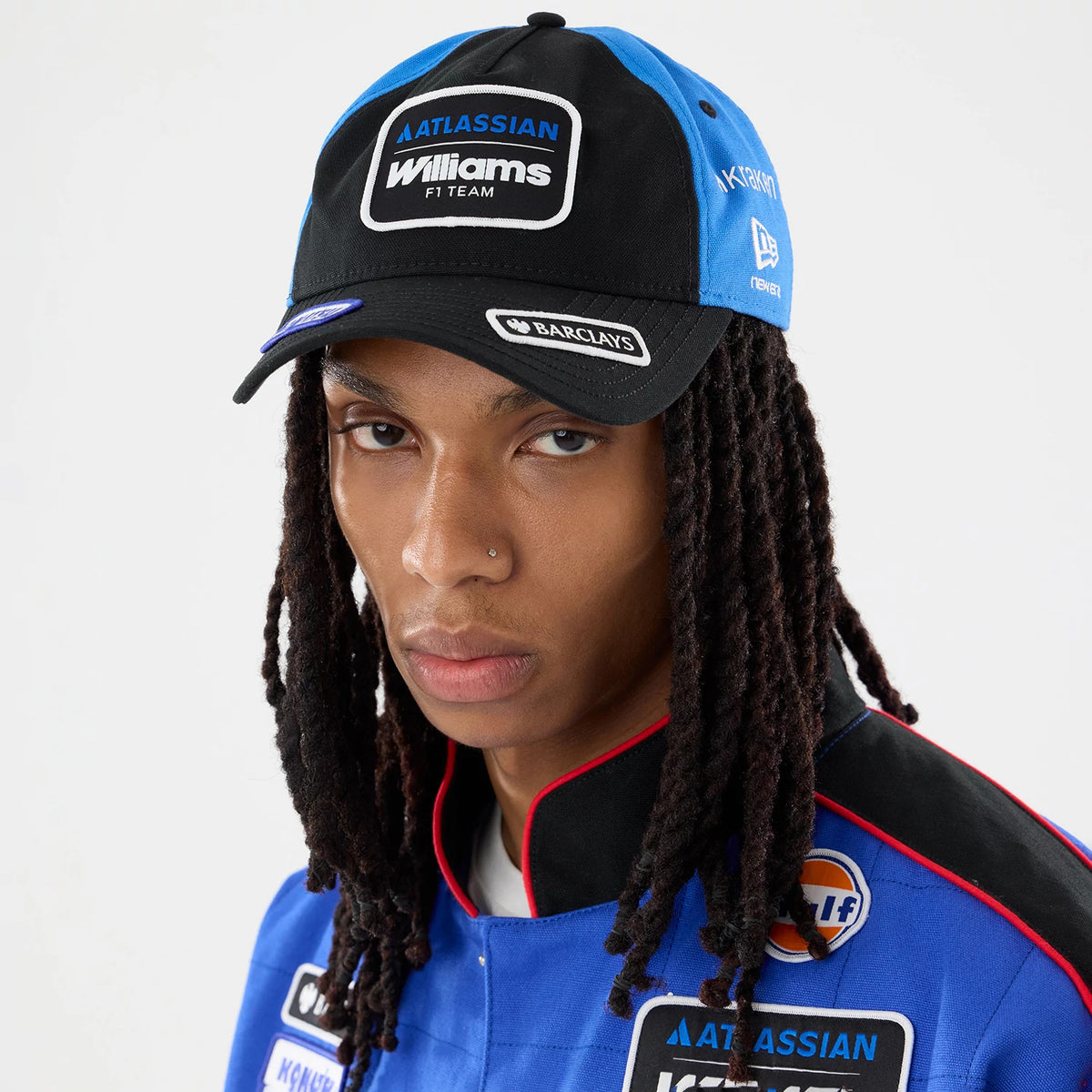 Williams Vegas Race Special Black New Era 9TWENTY A-Frame Adjustable Cap, front view on a model wearing a blue racing jacket, featuring a black visor, a rectangular embroidered Williams F1 Team logo patch, and the New Era flag on the blue side panel.