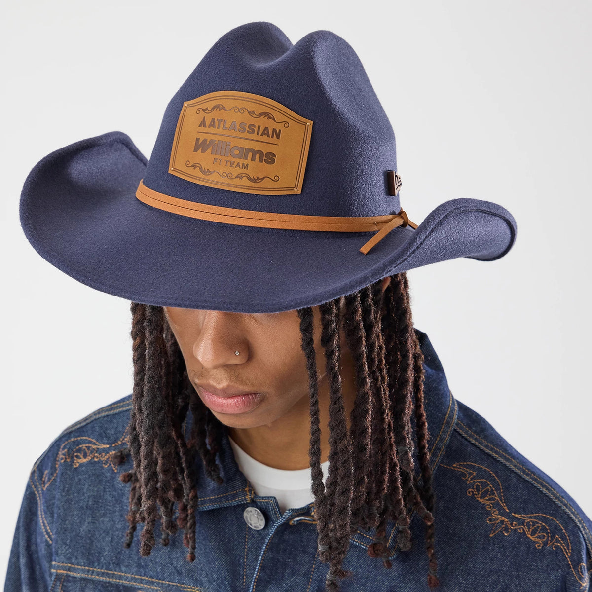 New Era Williams Austin Race Special Navy Wide Brim Fedora Cowboy Hat, on-model view with a large, decorative leather patch on the front, a thin brown hatband encircling the crown, and a distinctively shaped, wide visor.
