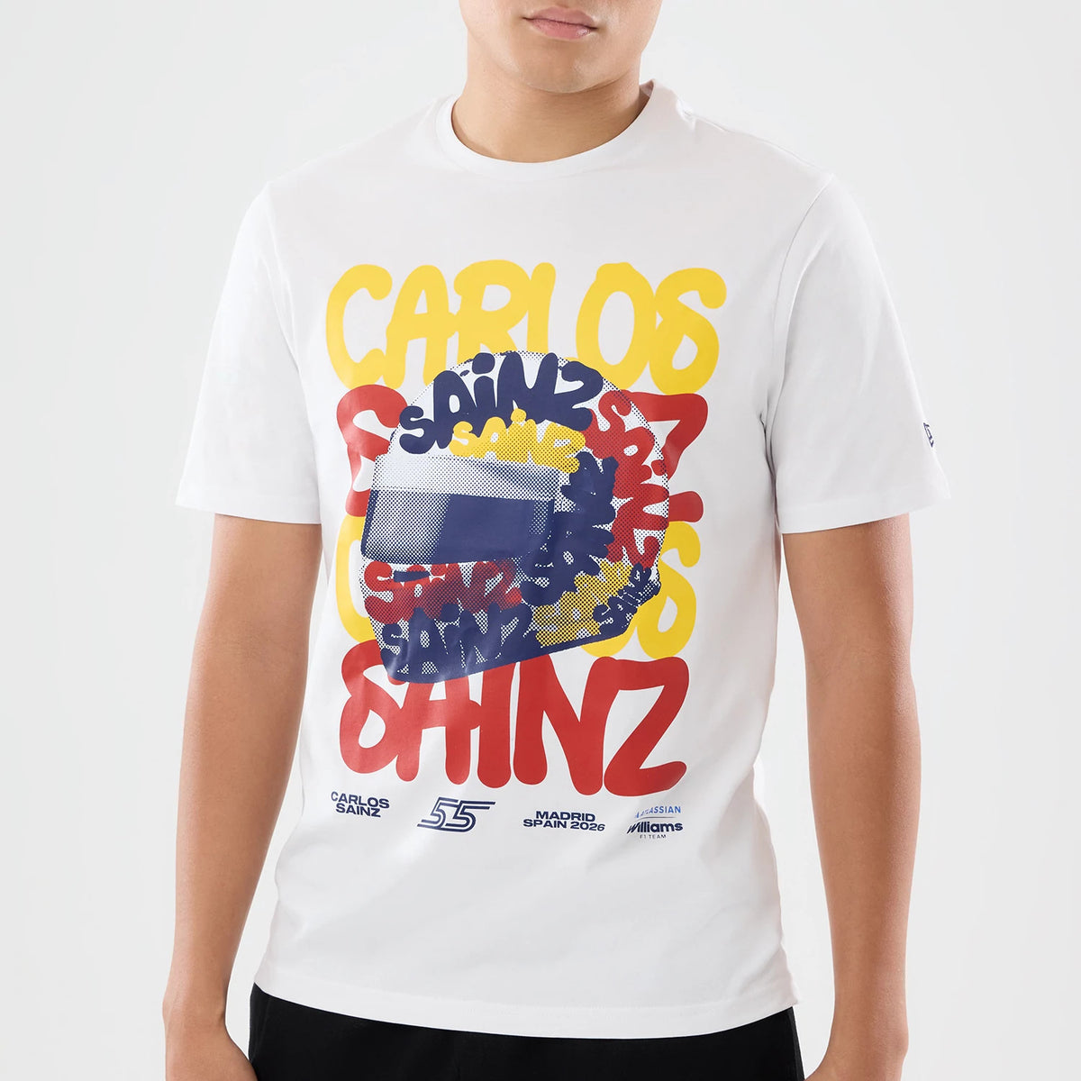 New Era Williams Carlos Sainz Spain Race Special White T-Shirt, front view on a model showing a large graphic design with overlapping yellow, blue, and red lettering with a stylised helmet pattern, and small logos printed near the hemline.