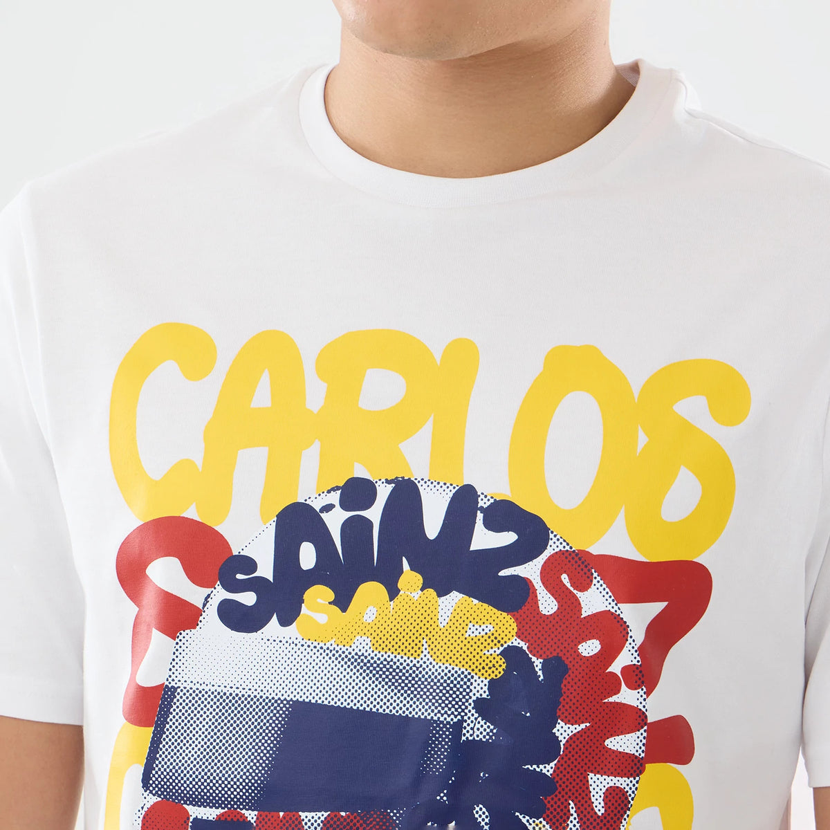New Era Williams Carlos Sainz Spain Race Special White T-Shirt, front view showing a design with yellow CARLOS lettering, repeated SAINZ in blue, surrounding a graphic of a helmet across the chest.