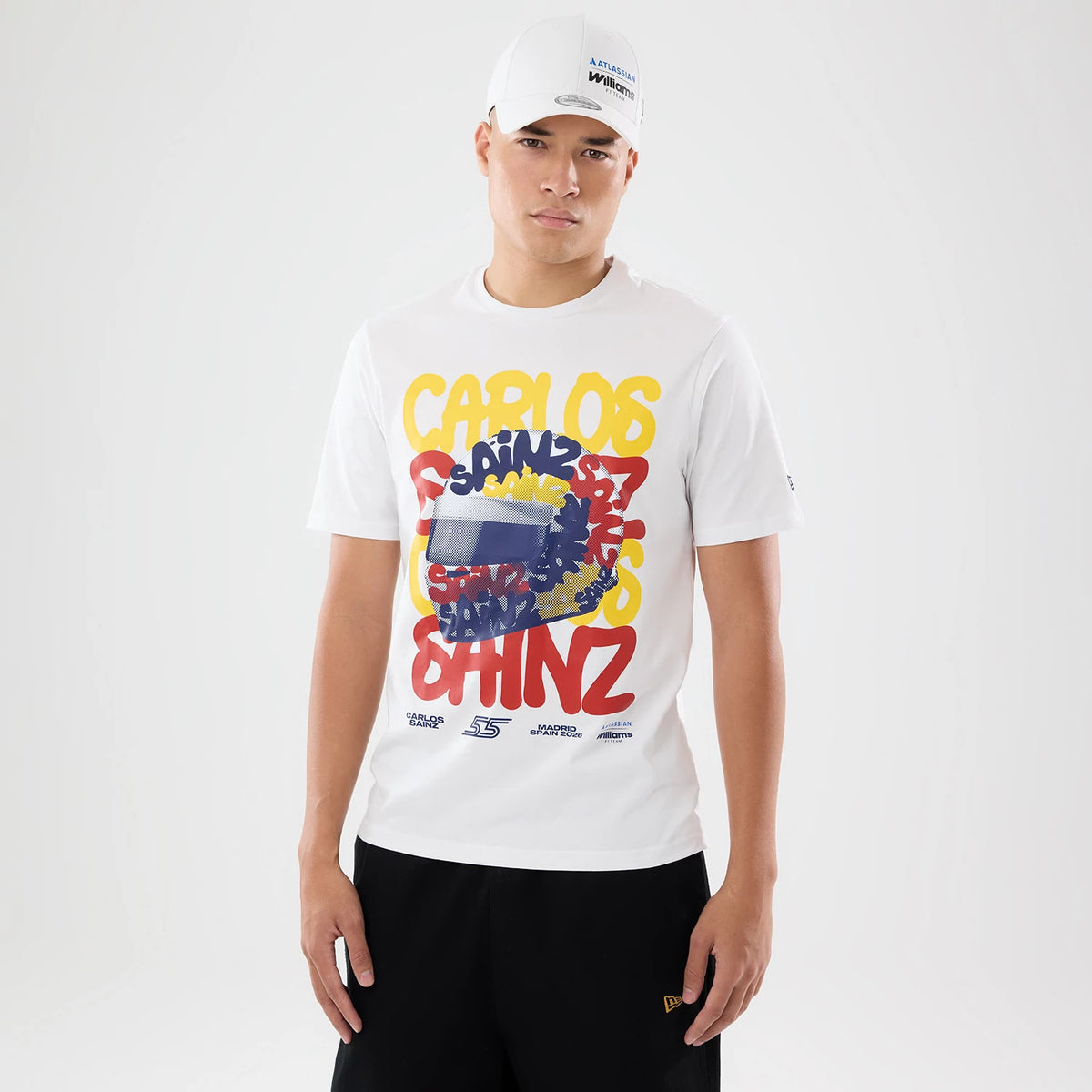 New Era Williams Carlos Sainz Spain Race Special White T-Shirt, front view on-model showing a graphic design with 'Carlos Sainz' in yellow, blue, and red letters, a New Era logo on the sleeve, paired with black shorts and a white cap.