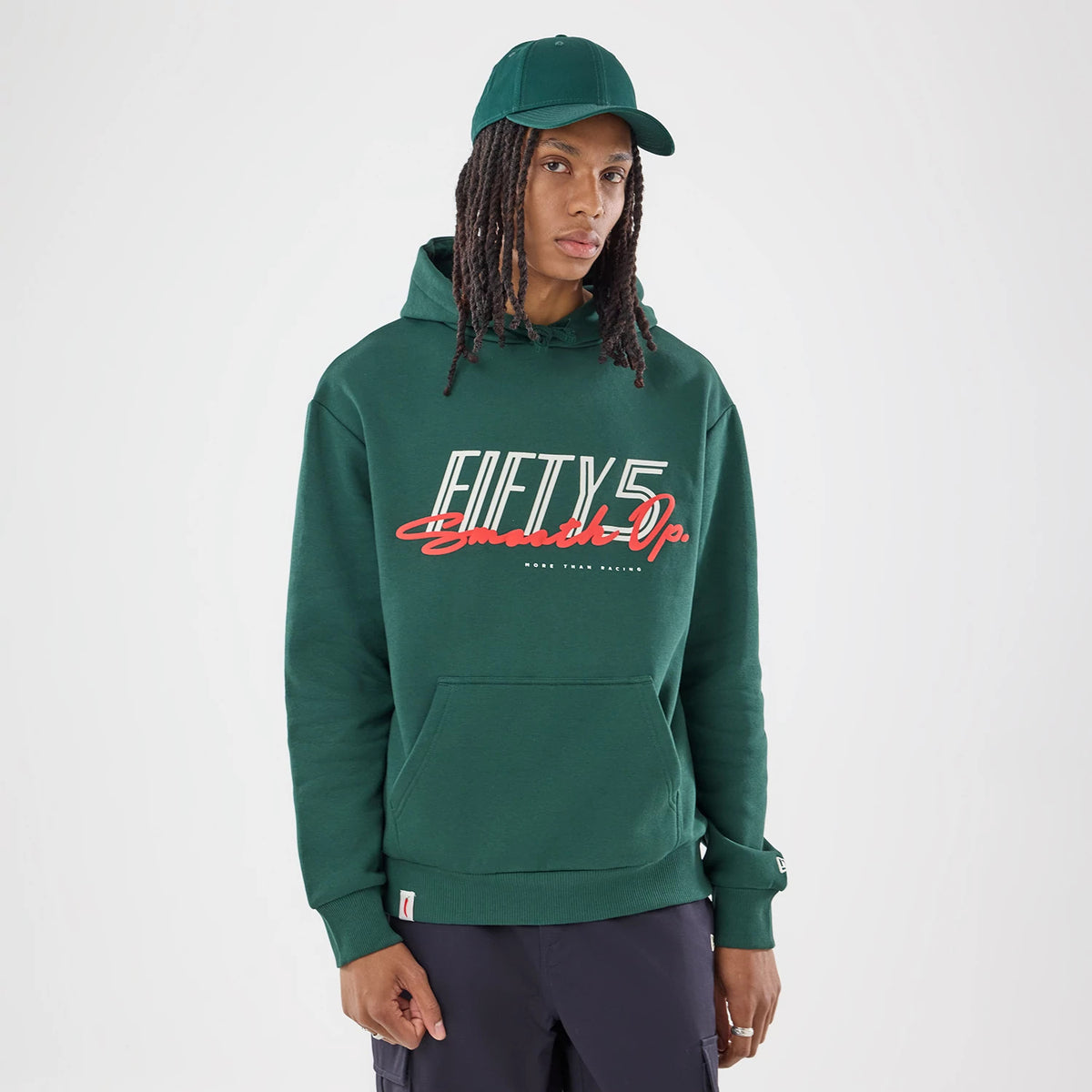 New Era Carlos Sainz Team Fifty5 Smooth Dark Green Oversized Pullover Hoodie, front view on a model wearing a matching cap, displaying white and red lettering across the chest, with a kangaroo pocket.
