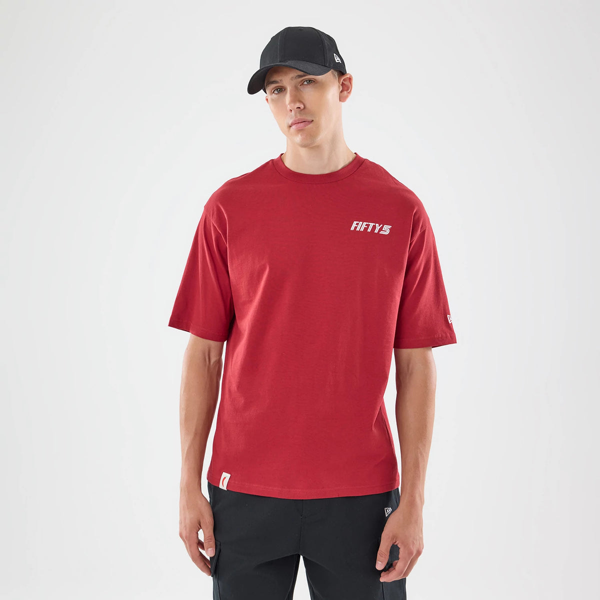 New Era Carlos Sainz Team Fifty5 Madrid Dark Red Oversized T-Shirt, front view on a model, displaying a white printed Fifty5 logo on the upper left chest, short sleeves, and a small embroidered New Era flag on the left sleeve.