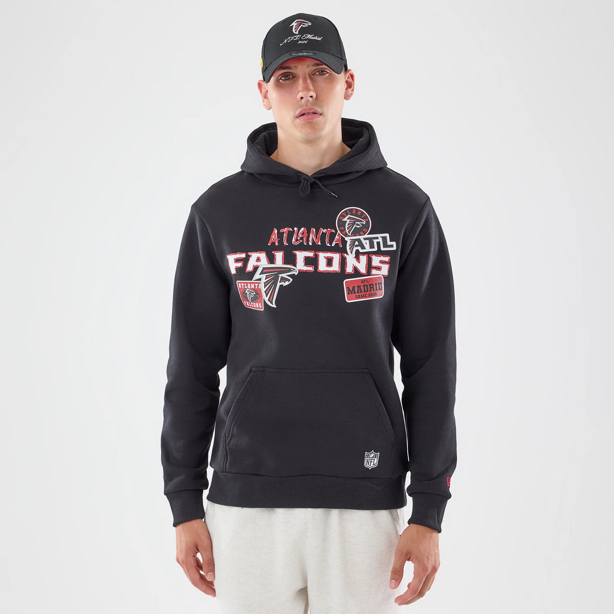 New Era Atlanta Falcons NFL Patch Black Pullover Hoodie, front view on a model styled with a cap, displaying multiple embroidered team patches on the chest, a central kangaroo pocket, and a small NFL logo near the hem.