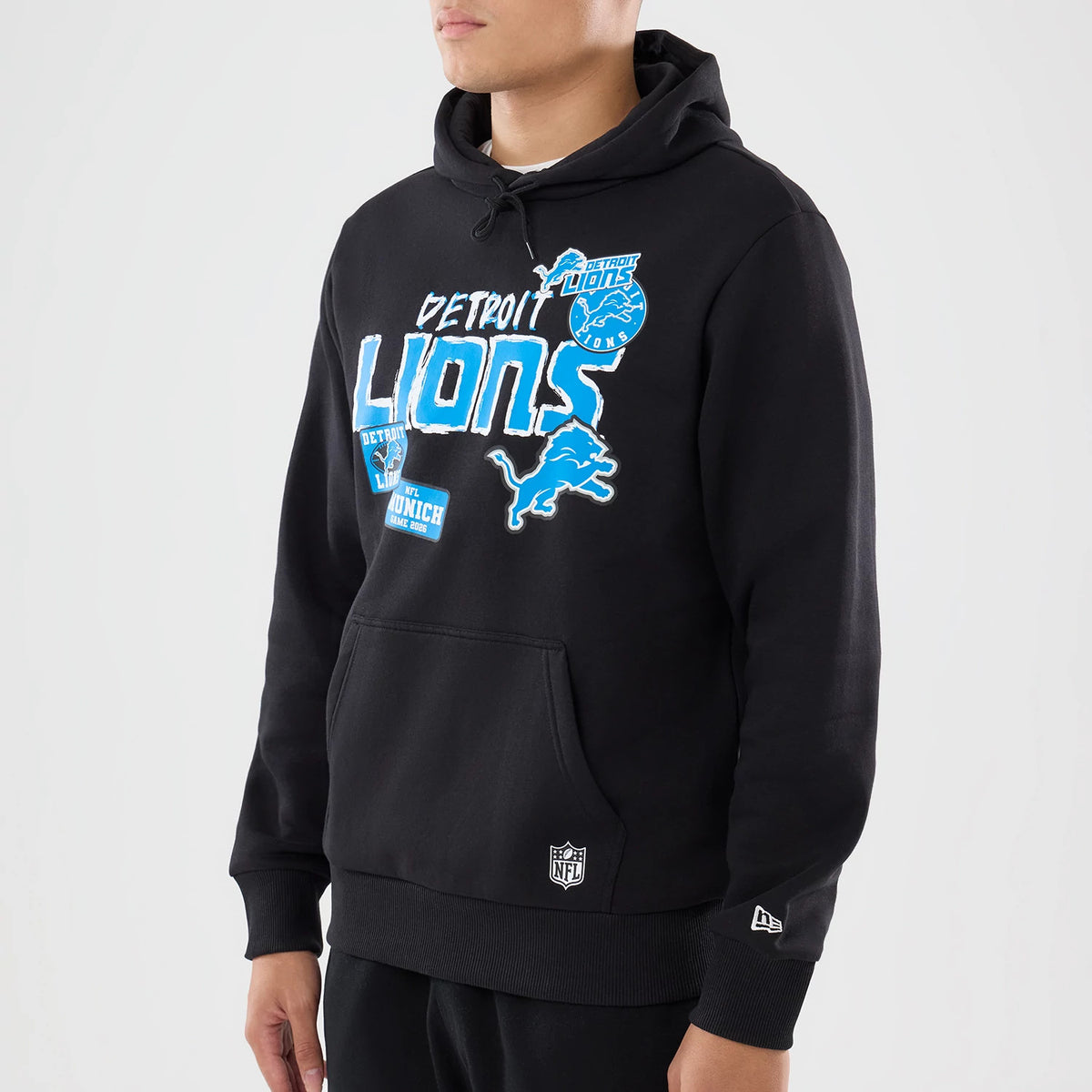 New Era Detroit Lions NFL Patch Black Pullover Hoodie, front view on a model showcasing blue and white Lions graphics and logos across the chest, a kangaroo pocket at the front, an embroidered NFL logo near the hem, and a New Era logo on the cuff.