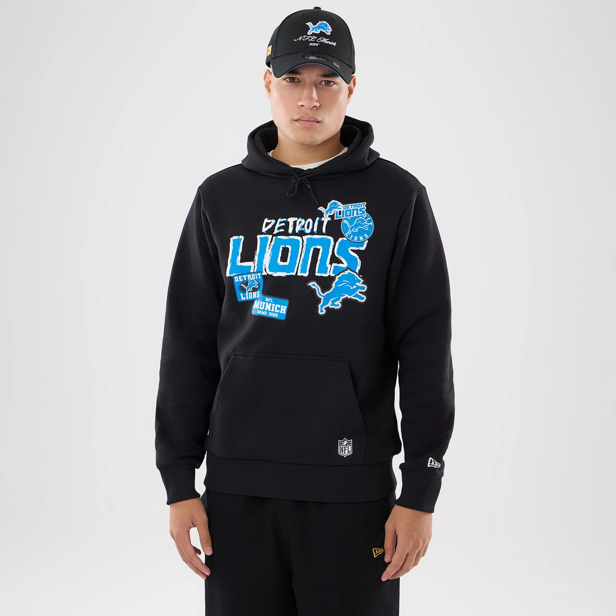 New Era Detroit Lions NFL Patch Black Pullover Hoodie, front view on-model showcasing blue and white Detroit Lions graphics across the chest, drawstrings at the neck, a small kangaroo pocket, and embroidered logos on the sleeves and hem.