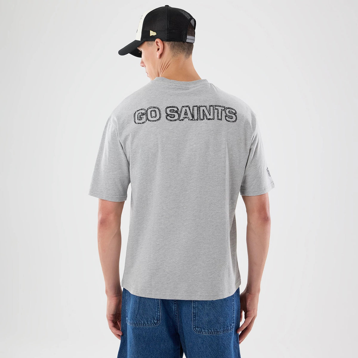 New Era New Orleans Saints NFL Graphic Slogan Grey Oversized T-Shirt, back view on-model displaying GO SAINTS lettering across the upper back in a printed design, short sleeves and a loose fit paired with casual jeans.
