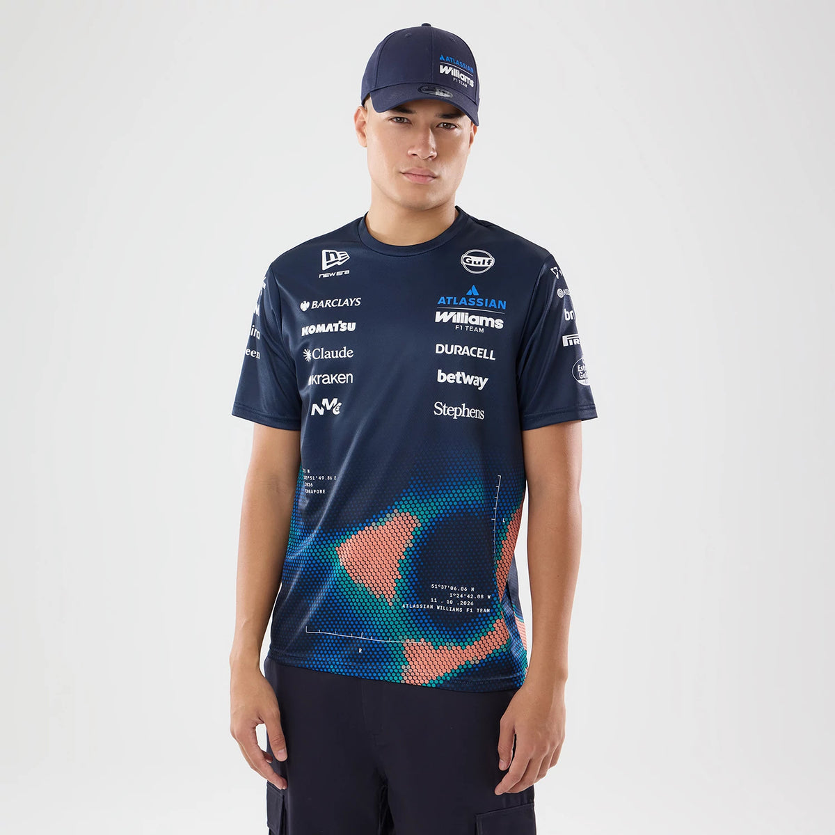 New Era Williams Singapore Navy Tech T-Shirt, front view on-model displaying a navy design with various embroidered sponsor logos across the chest and sleeves, along with a geometric pattern in shades of blue and orange on the lower front.