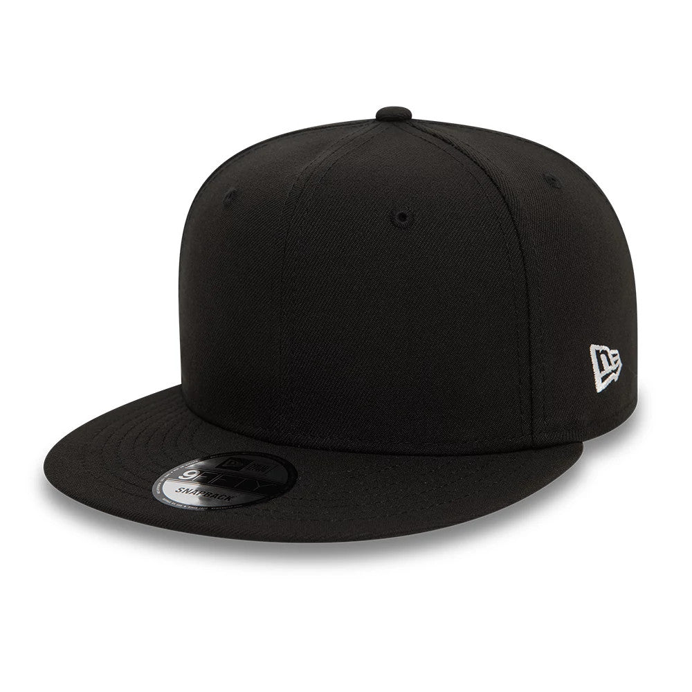 New Era Essential Black New Era 9FIFTY Snapback Cap, three-quarter view showing a white embroidered New Era flag logo on the left side, a flat black visor with a 9FIFTY size sticker, and a black structured crown.