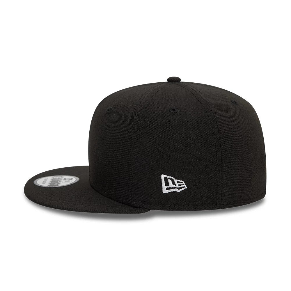 New Era Essential Black 9FIFTY Snapback Cap, side view showing the white embroidered New Era flag logo on the left side of the structured black crown, with a flat black visor and a 9FIFTY size sticker on top.