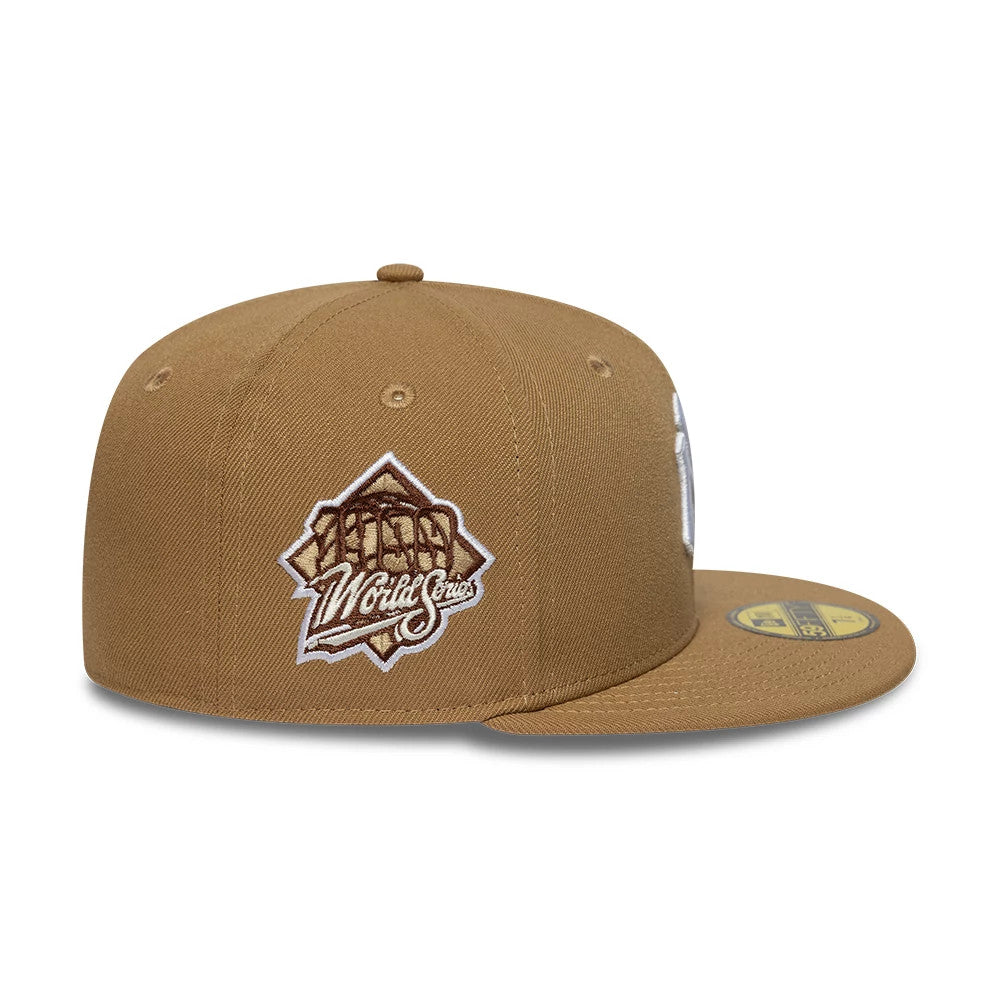 New York Yankees MLB Beige New Era 59FIFTY Fitted Cap, side view showing the World Series patch in brown and white embroidery on the structured beige crown, with a flat visor and the gold 59FIFTY size sticker on the top.
