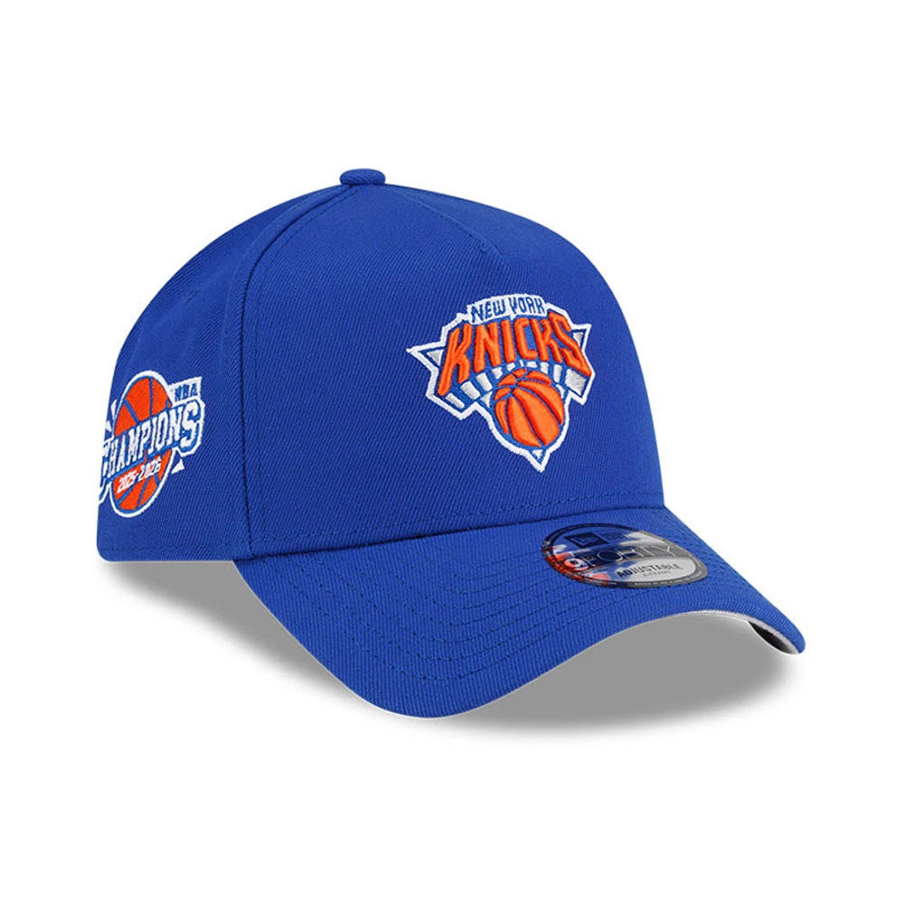 New York Knicks NBA Champs 2025 - 2026 Blue New Era 9FORTY A-Frame Adjustable Cap, three-quarter view showing the raised embroidered Knicks logo on the front panel, NBA Champions logo on the side, and a 9FORTY size sticker on the blue curved visor.