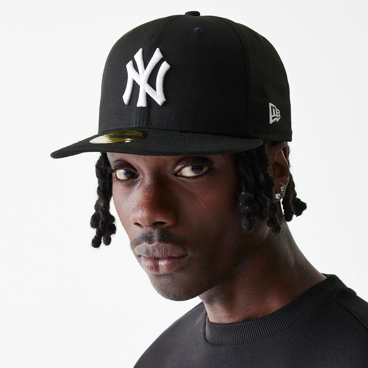 New York Yankees Essential Black New Era 59FIFTY Cap, front view on a model with a raised white NY logo on the front panel, New Era flag logo on the left side, and a gold 59FIFTY size sticker on the black visor.