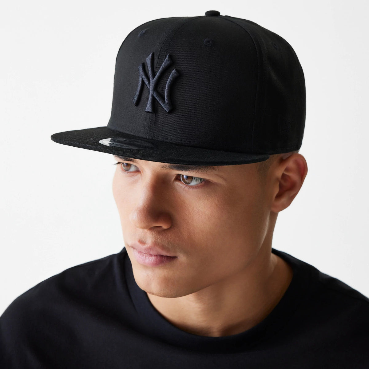 New York Yankees Black On Black New Era 9FIFTY Cap, on-model view with a raised black NY logo on the front panel and the 9FIFTY size sticker on the flat visor, paired with a black T-shirt.
