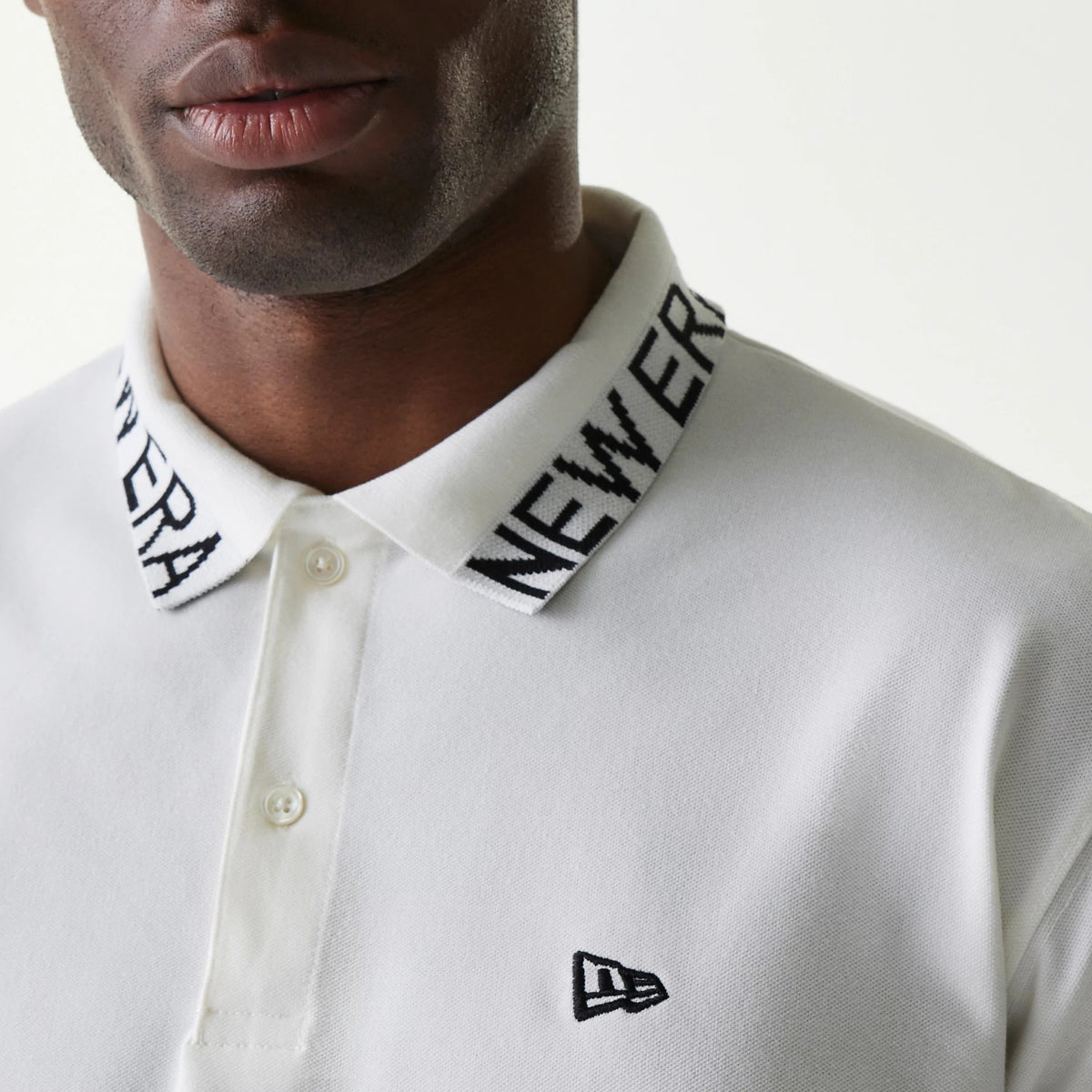 New Era Japan Collar Logo White Polo T-Shirt, front view showing the black embroidered New Era logo on the chest, a white buttoned placket, and a distinct collar featuring the black wordmark in a repeated design.