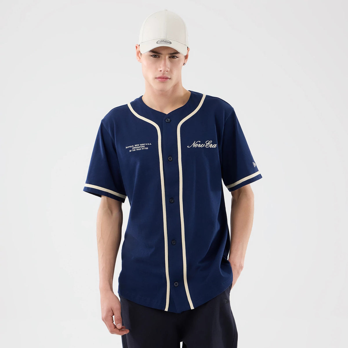 New Era Oceanside Blue Jersey, front view on a model wearing a light cap, showing the New Era script logo embroidered on the left chest and contrasting piping details along the neckline and button placket.