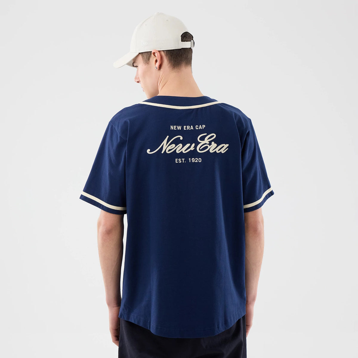 New Era Oceanside Blue Jersey, back view on a model featuring a large white New Era logo with "EST. 1920" text centred on the upper back, highlighted by white piping along the sleeves and neckline.