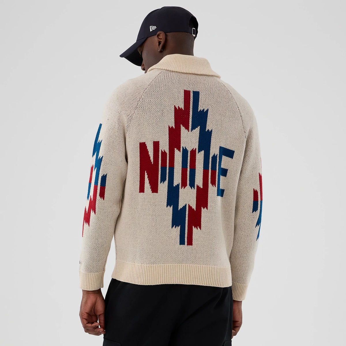 New Era Organic Cowichan Natural Cardigan, back view on a model wearing a black cap, showcasing a large red, white and blue geometric pattern with N love E lettering across the back and sleeves.