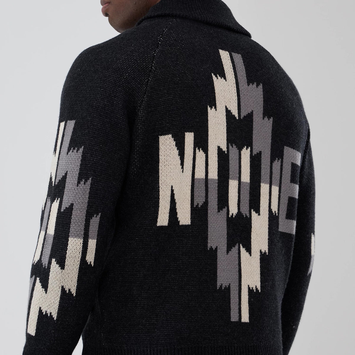 New Era Organic Cowichan Black Cardigan, rear view on a model showing a bold geometric pattern in beige and grey extending across the back and sleeves, with a high collar and ribbed cuffs.