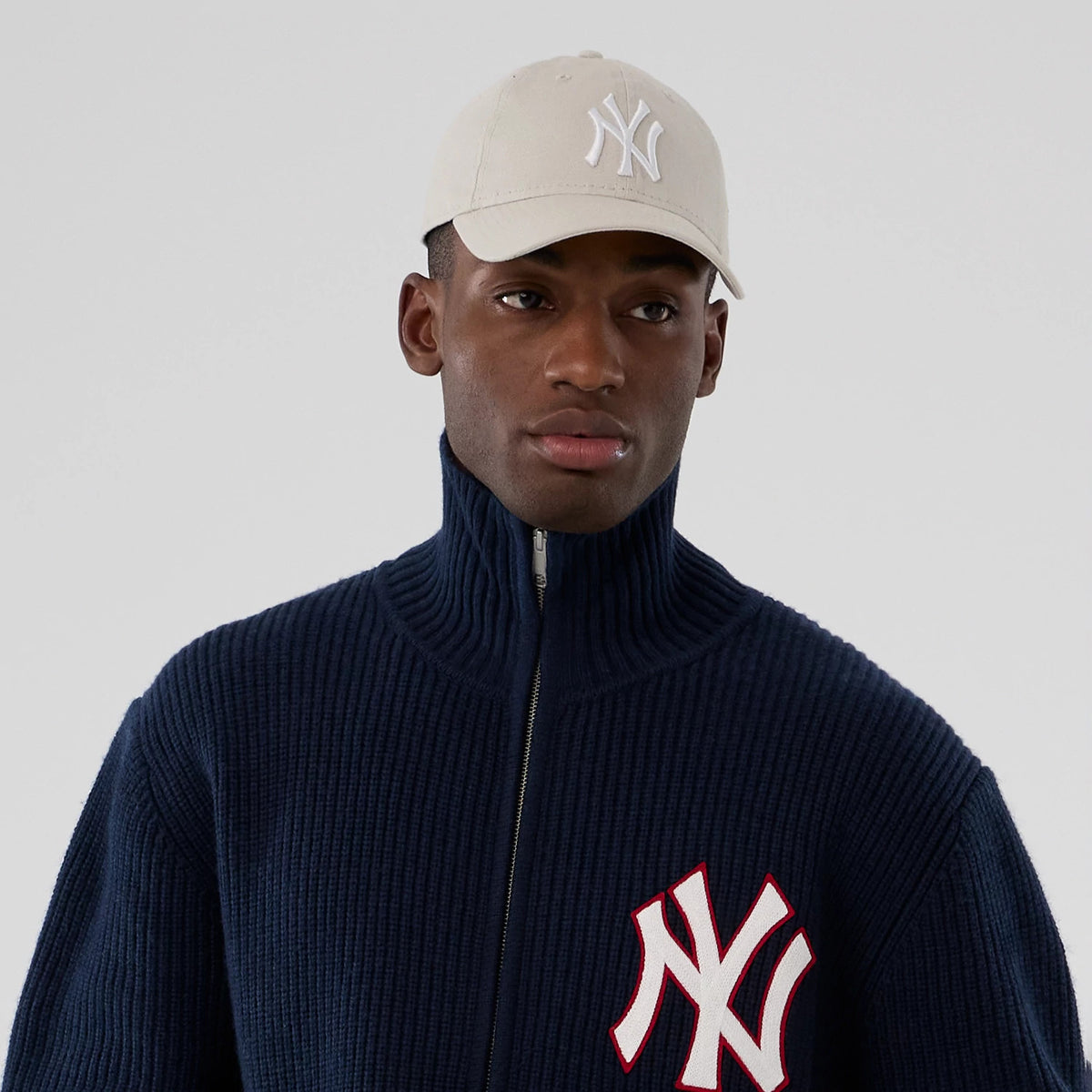 New York Yankees MLB Navy Cardigan, on-model view with a navy cardigan featuring a white and red embroidered NY logo on the left chest, paired with a beige cap showing a white embroidered NY logo on the front panel.