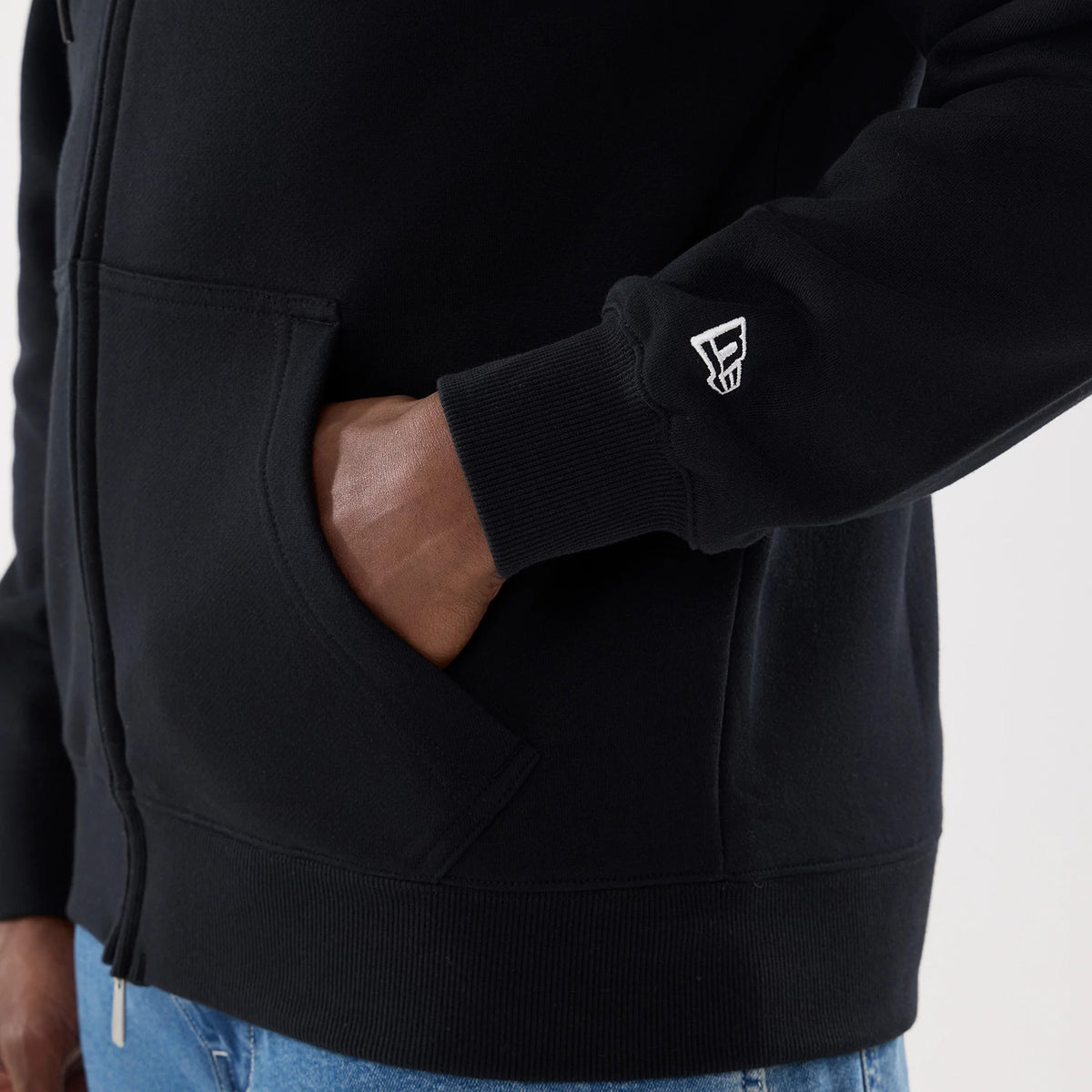 Las Vegas Raiders NFL Word Art Black 2 Way Full Zip Hoodie, side view showing the black fabric with a hand in the pocket, a raised logo on the cuff, and the full zip extending from the hem up the front.