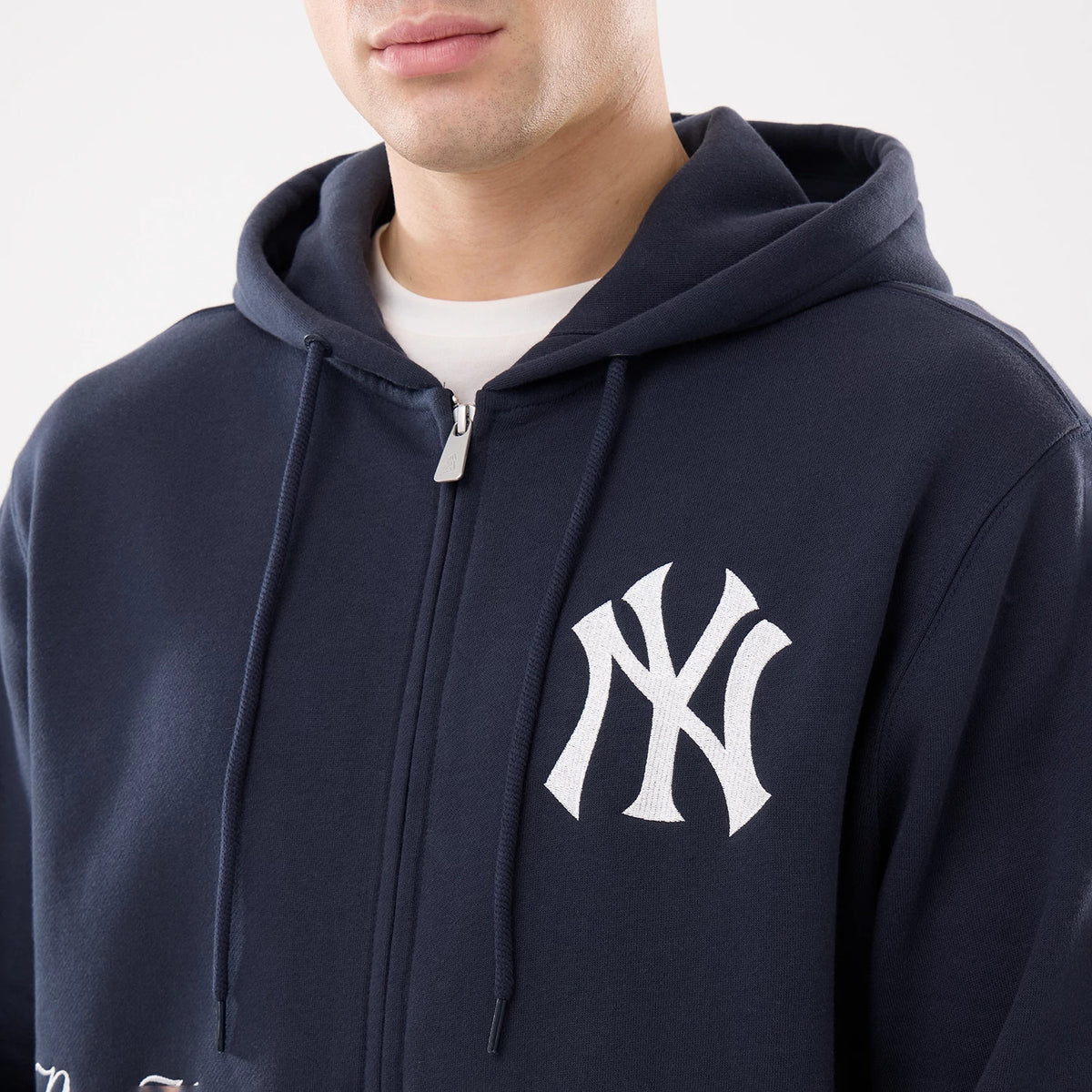 New York Yankees MLB Comfort Navy 2 Way Full Zip Hoodie, front view showing the navy hoodie with a white embroidered New York Yankees logo on the left chest, a full zip closure running down the front, and adjustable drawstrings on the hood.