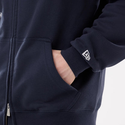 New York Yankees MLB Comfort Navy 2 Way Full Zip Hoodie, side view showing the ribbed cuff with a white raised New Era logo, a hand partially in one of the front pockets on the navy fabric and a visible part of the zip at the bottom.