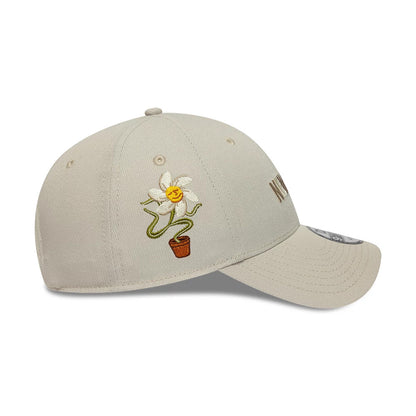 New Era Earth Day Beige 9FORTY Adjustable Cap, side view showing a colourful embroidered flower in a pot on the front panel and the New Era flag logo on the left side, with a curved visor featuring a 9FORTY size sticker.
