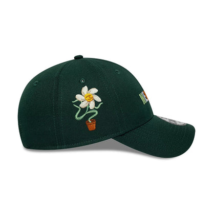 New Era Earth Day Dark Green 9FORTY Adjustable Cap, side view showing a white daisy with a yellow centre in a brown pot embroidered on the front panel, and the New Era flag logo in multicolour on the left side.
