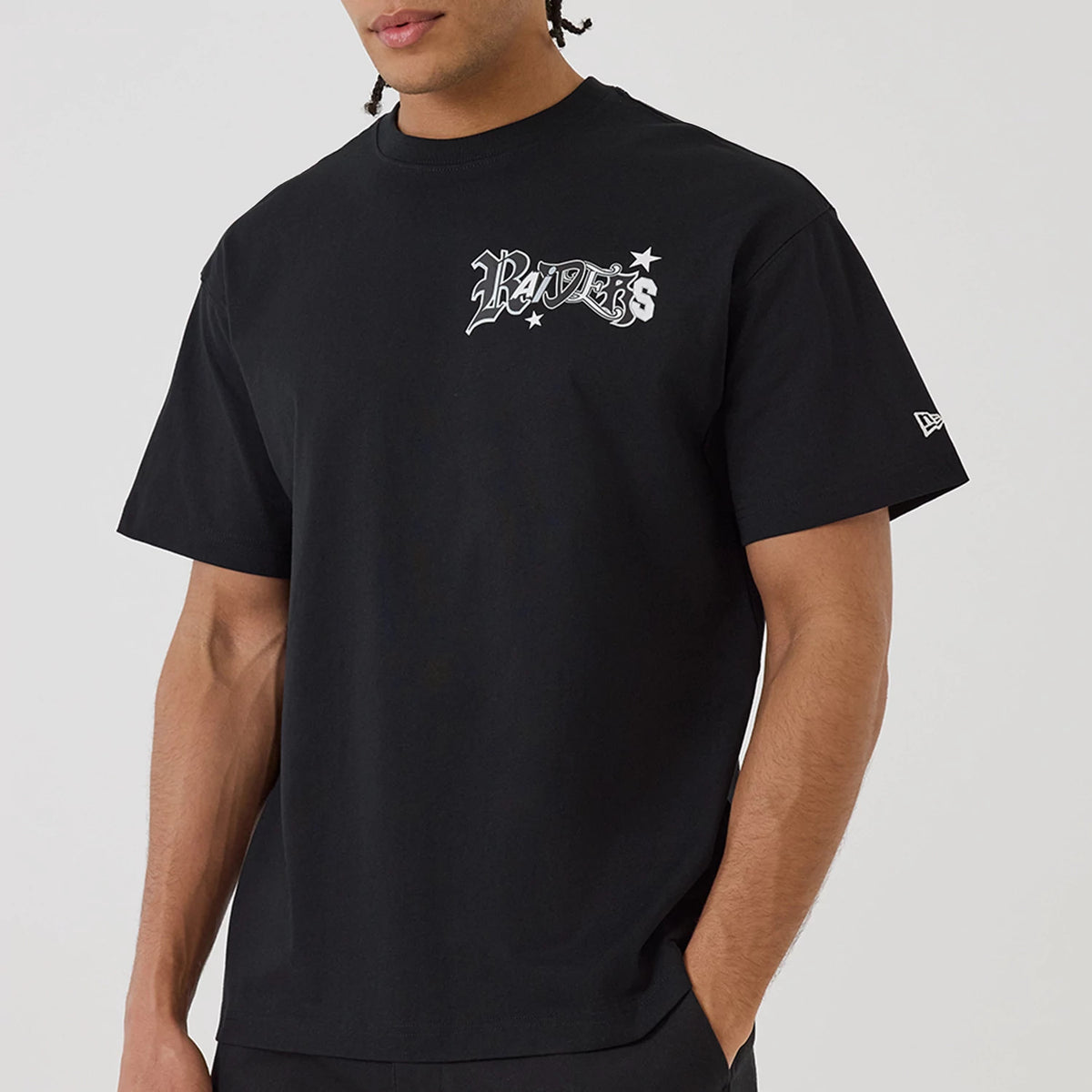Las Vegas Raiders NFL Word Art Black T-Shirt, on-model view showing the black shirt with 'Raiders' in white word art on the left chest and a white embroidered New Era logo on the left sleeve near the cuff.