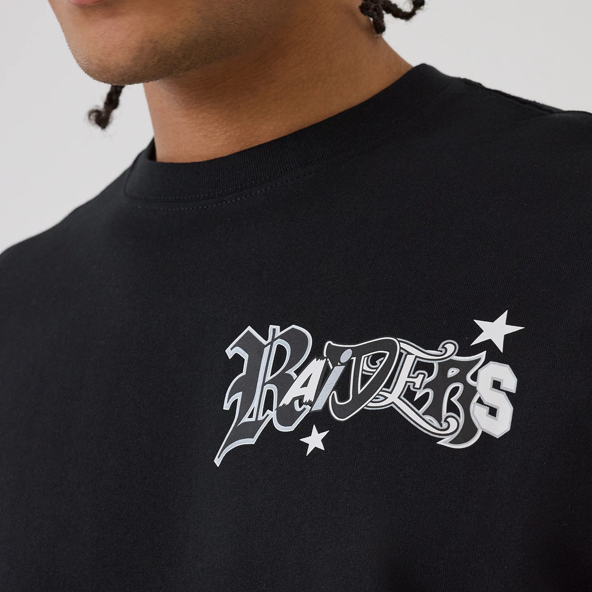 Las Vegas Raiders NFL Word Art Black T-Shirt, side view showing the black fabric with an embossed Raiders word art logo in white and grey on the upper chest, featuring two stars surrounding the text.