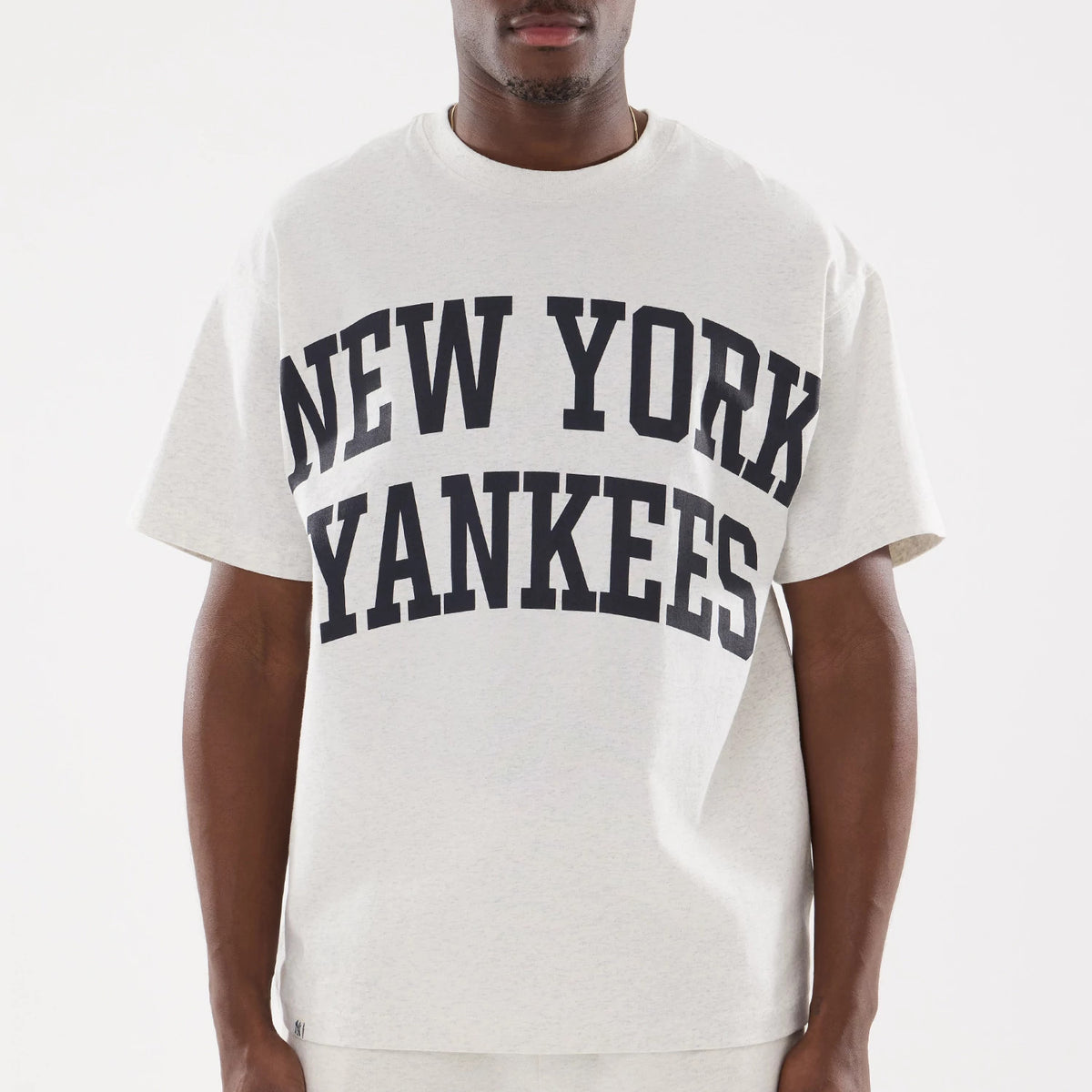 New York Yankees MLB Comfort Grey T-Shirt, front view showing large navy text across the chest reading "New York Yankees" on a light grey background, worn by a person standing with arms relaxed at their sides.