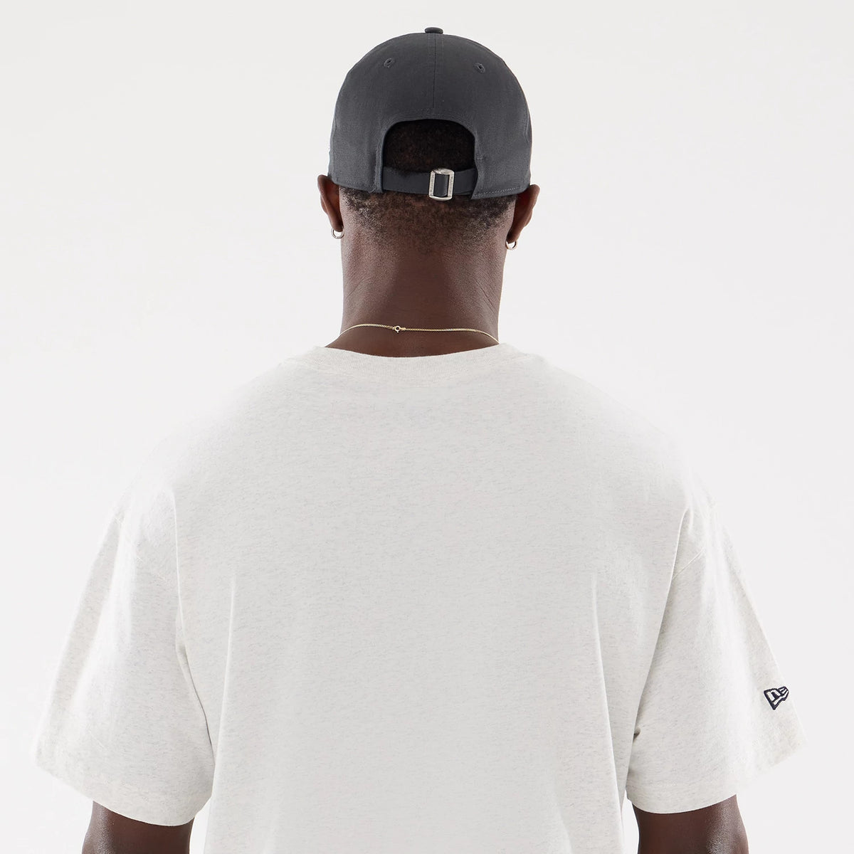 New Era New York Yankees MLB Comfort Grey T-Shirt, rear view showing a plain grey fabric with a short-sleeved design, a debossed New Era logo on the left sleeve, and a grey cap with eyelets worn by the model.