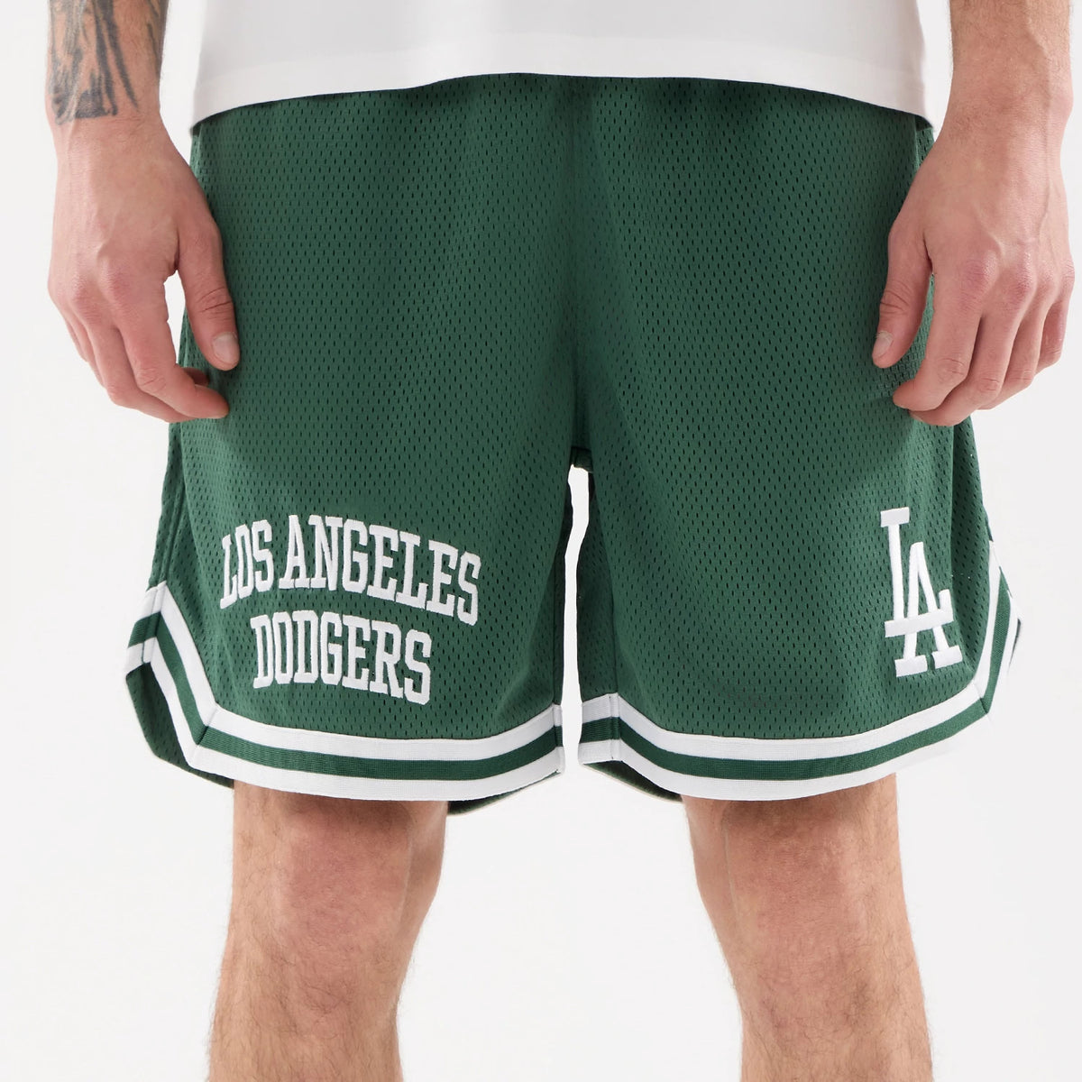 LA Dodgers MLB Comfort Dark Green Oversized Shorts, front view showing the white Los Angeles Dodgers text on the left leg, the white LA logo on the right leg, and double white stripes along the hem.
