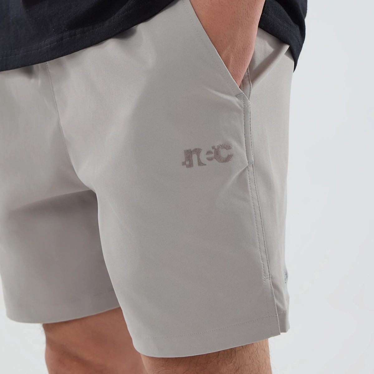 New Era NEC Logo Beige Oversized Shorts, side view showing a relaxed fit with a debossed NEC logo on the left thigh in a darker beige shade, and an angled side pocket above the logo.