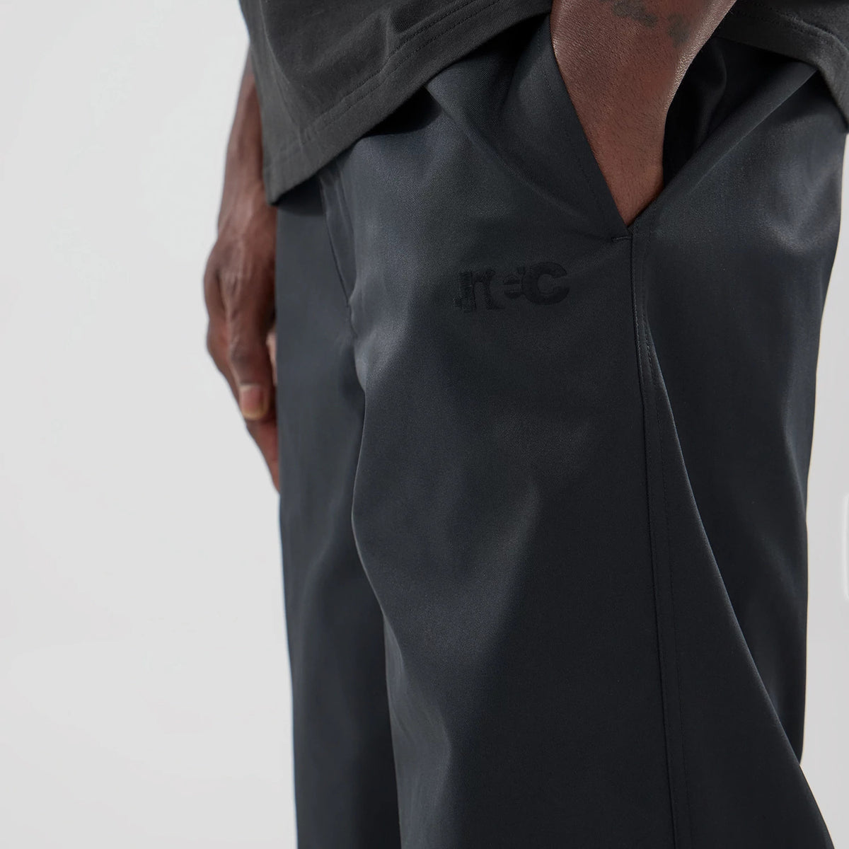 New Era NEC Logo Black Straight Leg Joggers, close-up showing a black tonal NEC logo embroidered near the right pocket seam, with a hand placed in the pocket, highlighting the smooth fabric texture and straight cut design.