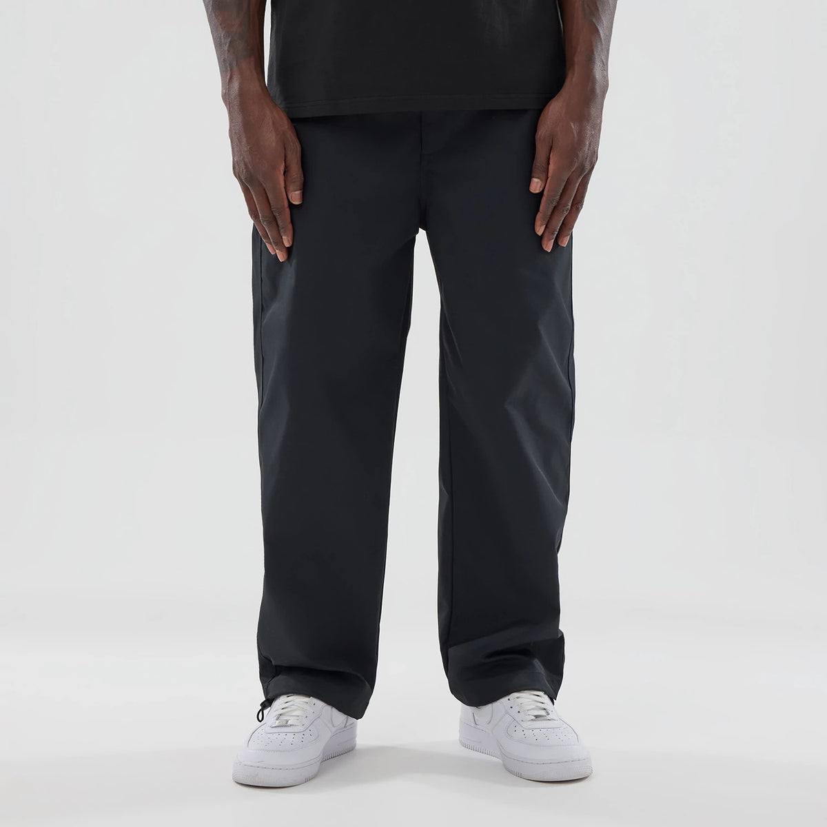New Era NEC Logo Black Straight Leg Joggers, front view on a model wearing white trainers and a black top, highlighting the relaxed fit and simple waistband with drawstring cuffs at the ankles.