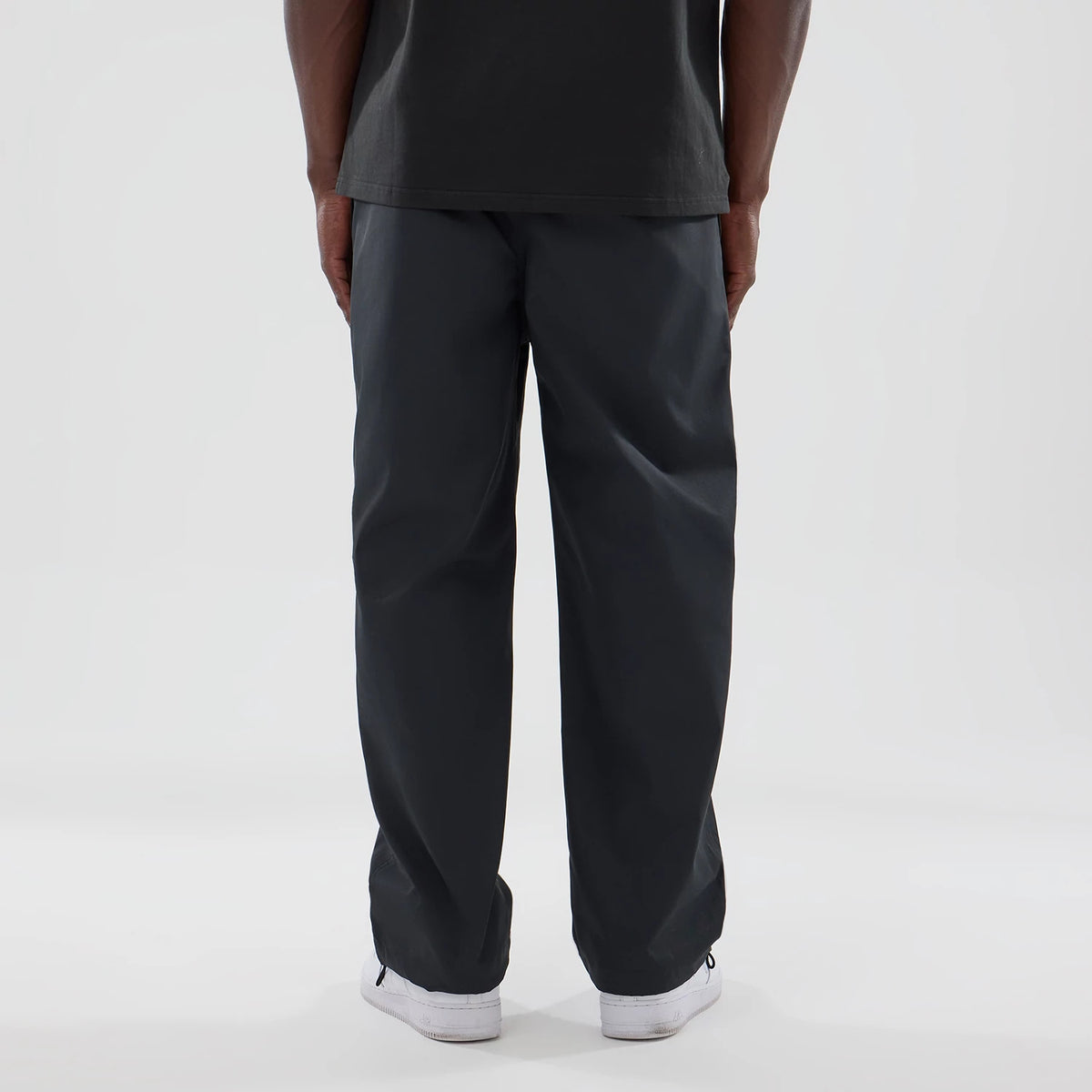 New Era NEC Logo Black Straight Leg Joggers, rear view on a model showing the relaxed fit and black fabric, paired with a black top and white sneakers, highlighting the joggers' straight leg design.