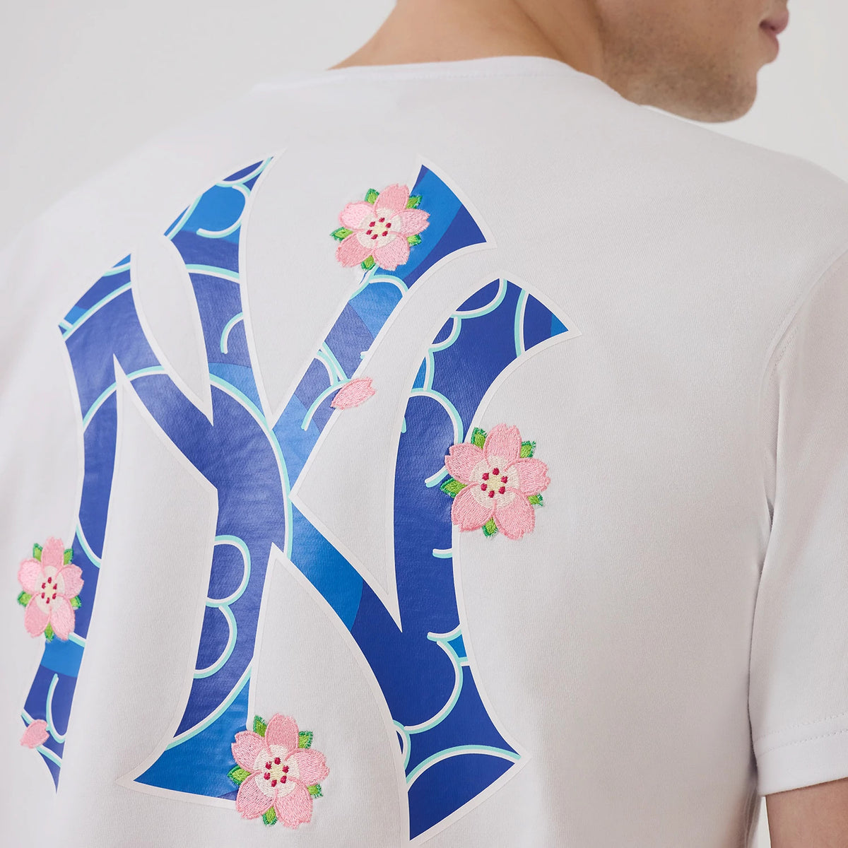 New York Yankees MLB Sakura White T-Shirt, rear view showcasing a large blue and white New Era logo with pink embroidered sakura flowers surrounding it on the back of the white fabric.