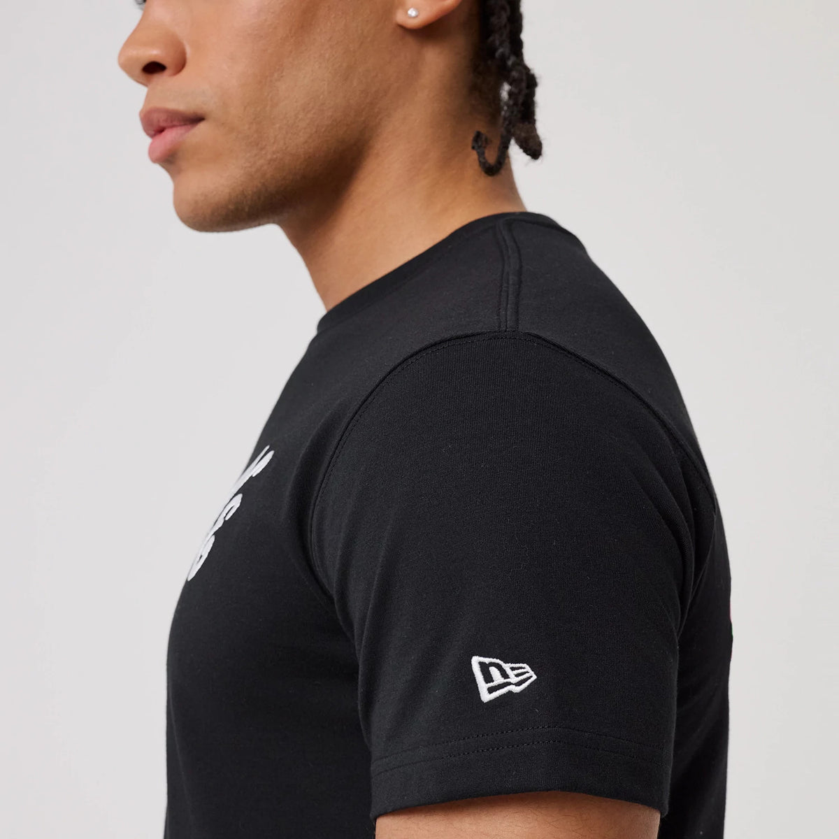 New Era Sakura Black T-Shirt, side view showing the black short sleeve with a raised white New Era logo near the hem, worn by a person with a close-fitting design and black stitching along the seams.