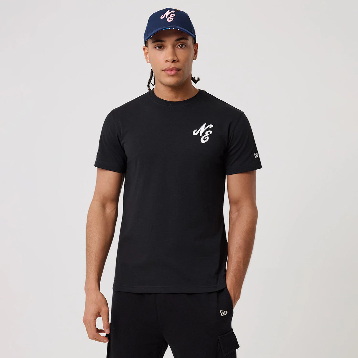 New Era Sakura Black T-Shirt, on-model view showing a man wearing a black T-shirt with a white raised logo on the chest, the New Era logo on the sleeve and a navy cap with the same logo on the front.
