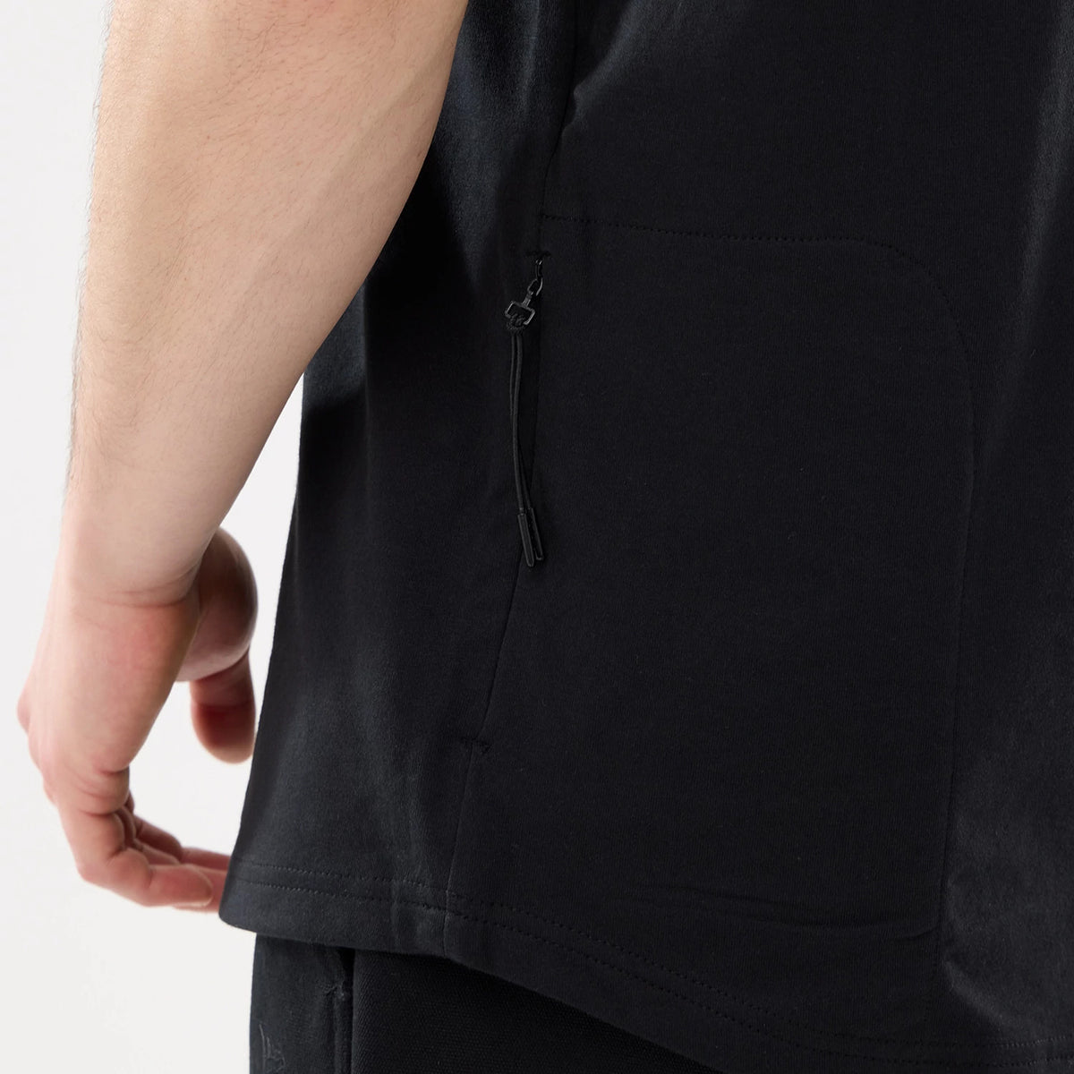 New Era Outdoor Mountain Black T-Shirt, side view showing the black fabric with a zip pocket running vertically along the side seam and a straight hem, demonstrating a relaxed fit on the lower body.