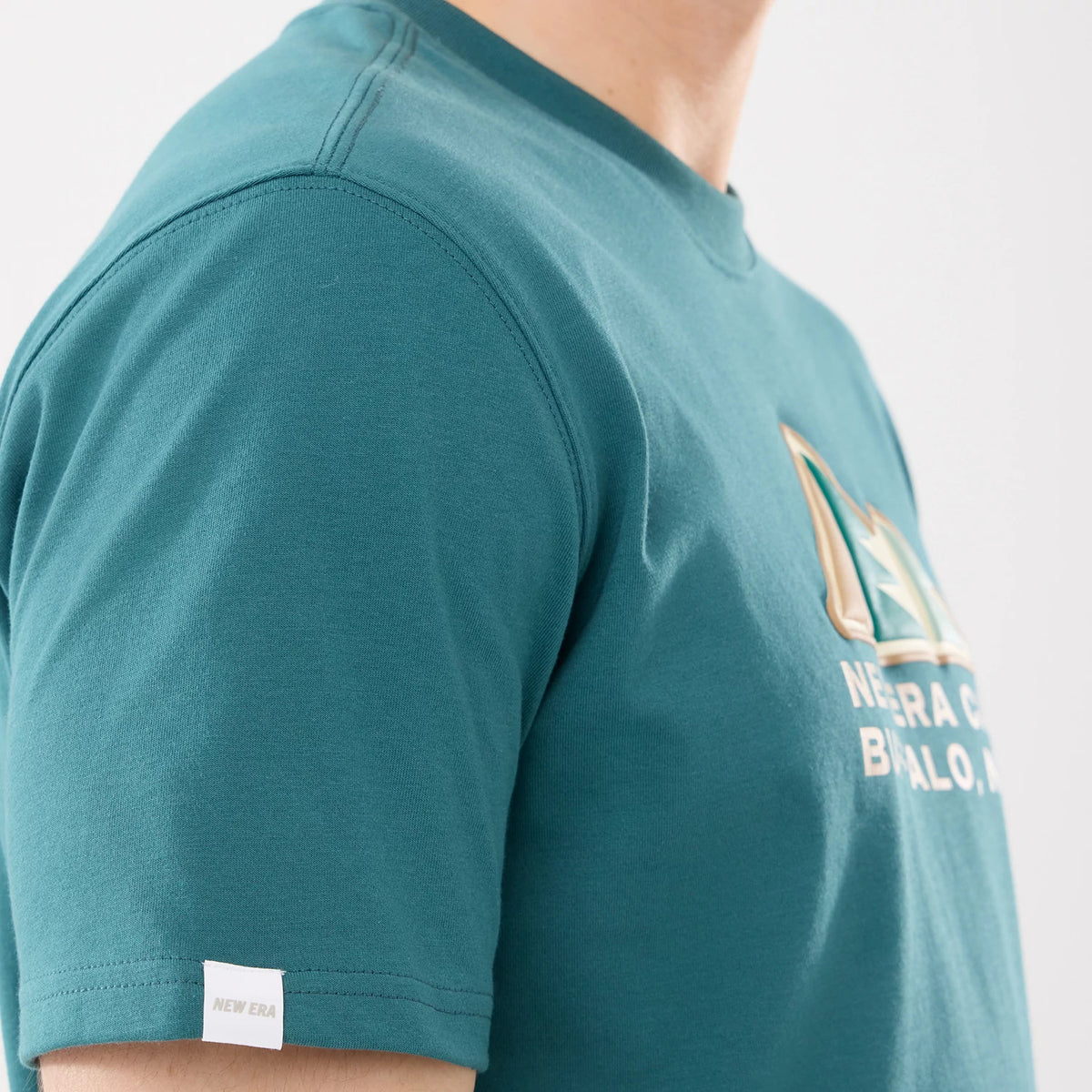 New Era Outdoor Mountain Dark Green T-Shirt, on-model view showing a dark green short sleeve with a small white New Era tag near the hem and a raised graphic logo on the chest featuring text and mountain design.