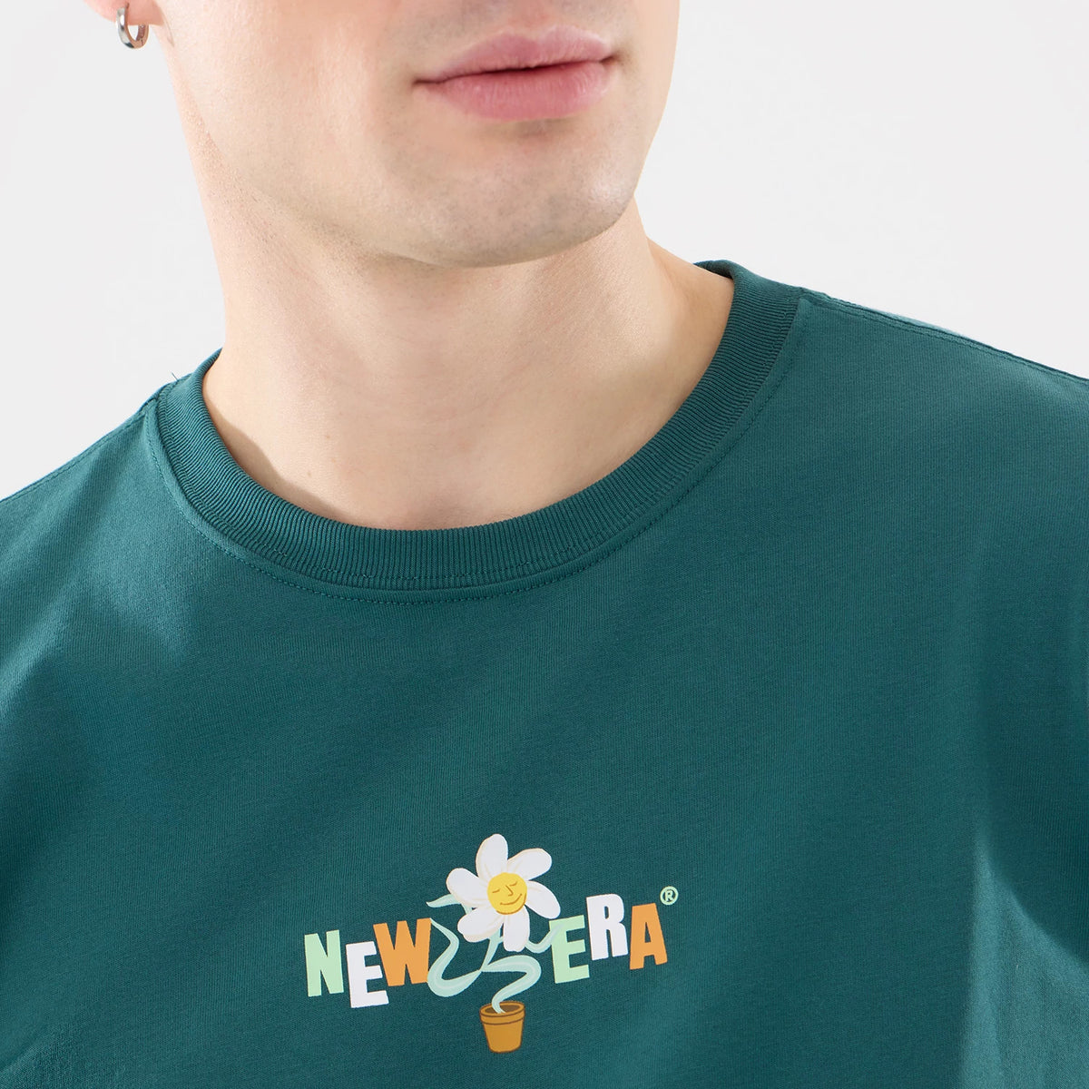 New Era Earth Day Dark Green T-Shirt, front view featuring a graphic with a smiling flower and the word "NEW ERA" in colourful letters, centred on the chest of the dark green fabric with a round neckline.