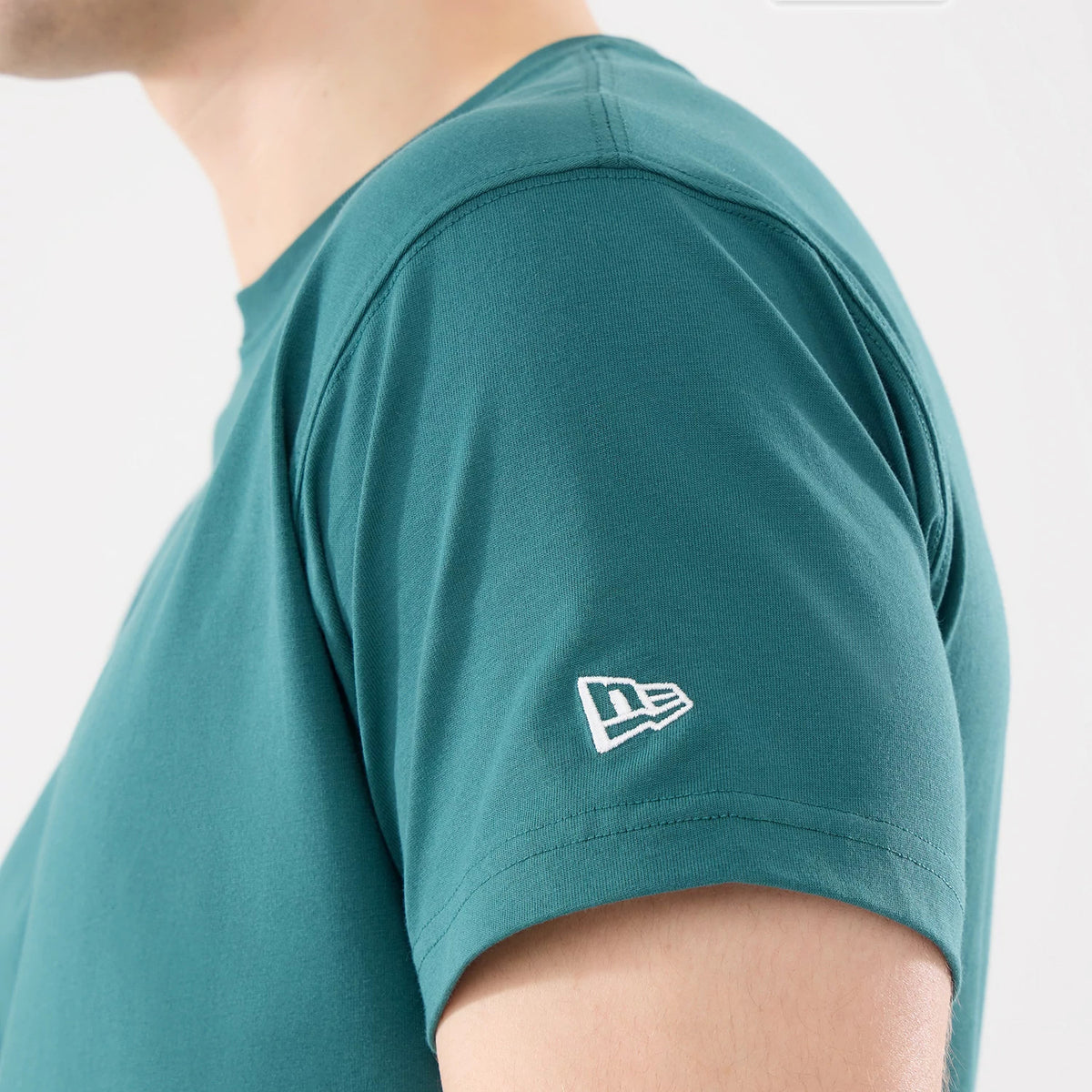New Era Earth Day Dark Green T-Shirt, side view showing the short sleeve with a white embroidered New Era logo on the upper left arm and a smooth neckline, highlighting the rich dark green fabric.