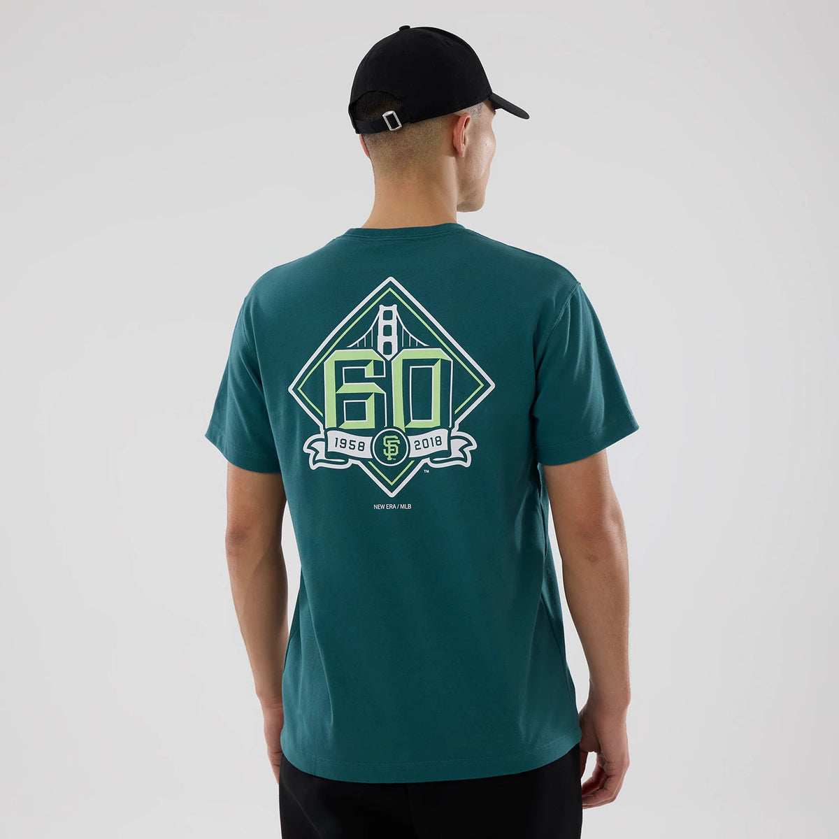 San Francisco Giants MLB Garden Dark Green T-Shirt, rear view showing a large graphic featuring the number 60 and the Golden Gate Bridge design in green and white on the back, worn by a person in a black cap.